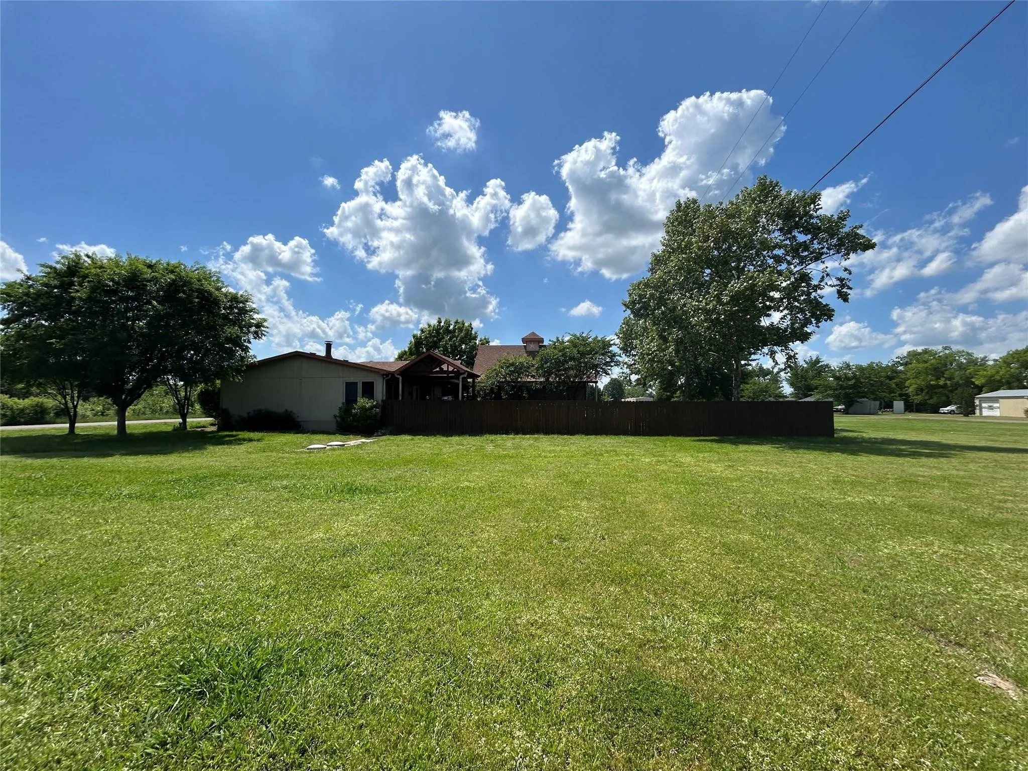 Expansive green lawn with mature trees and a privacy fence