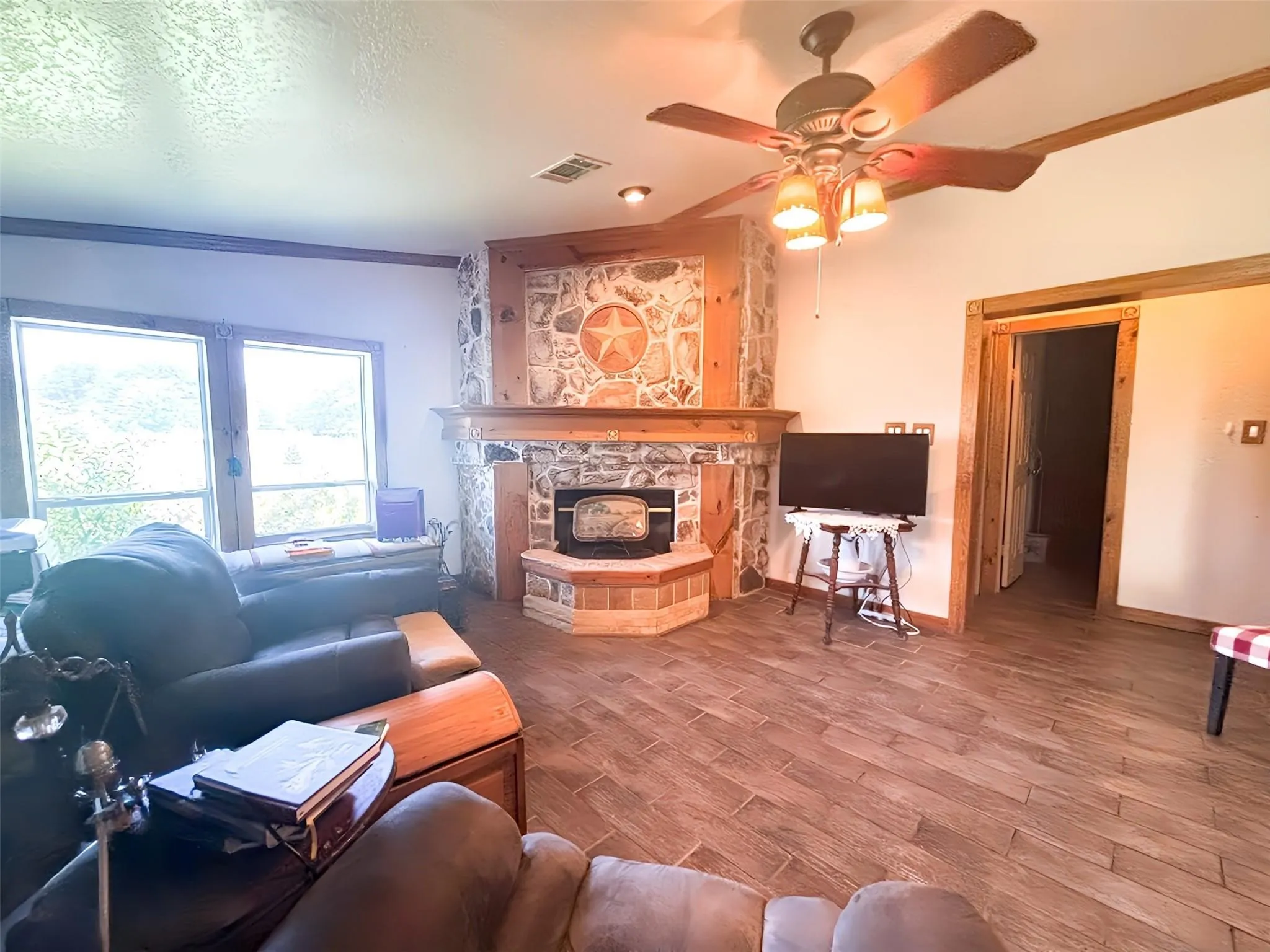 Living area featuring a stone-clad fireplace with wood mantel, wood-finish flooring, and a ceiling fan with integrated lighting