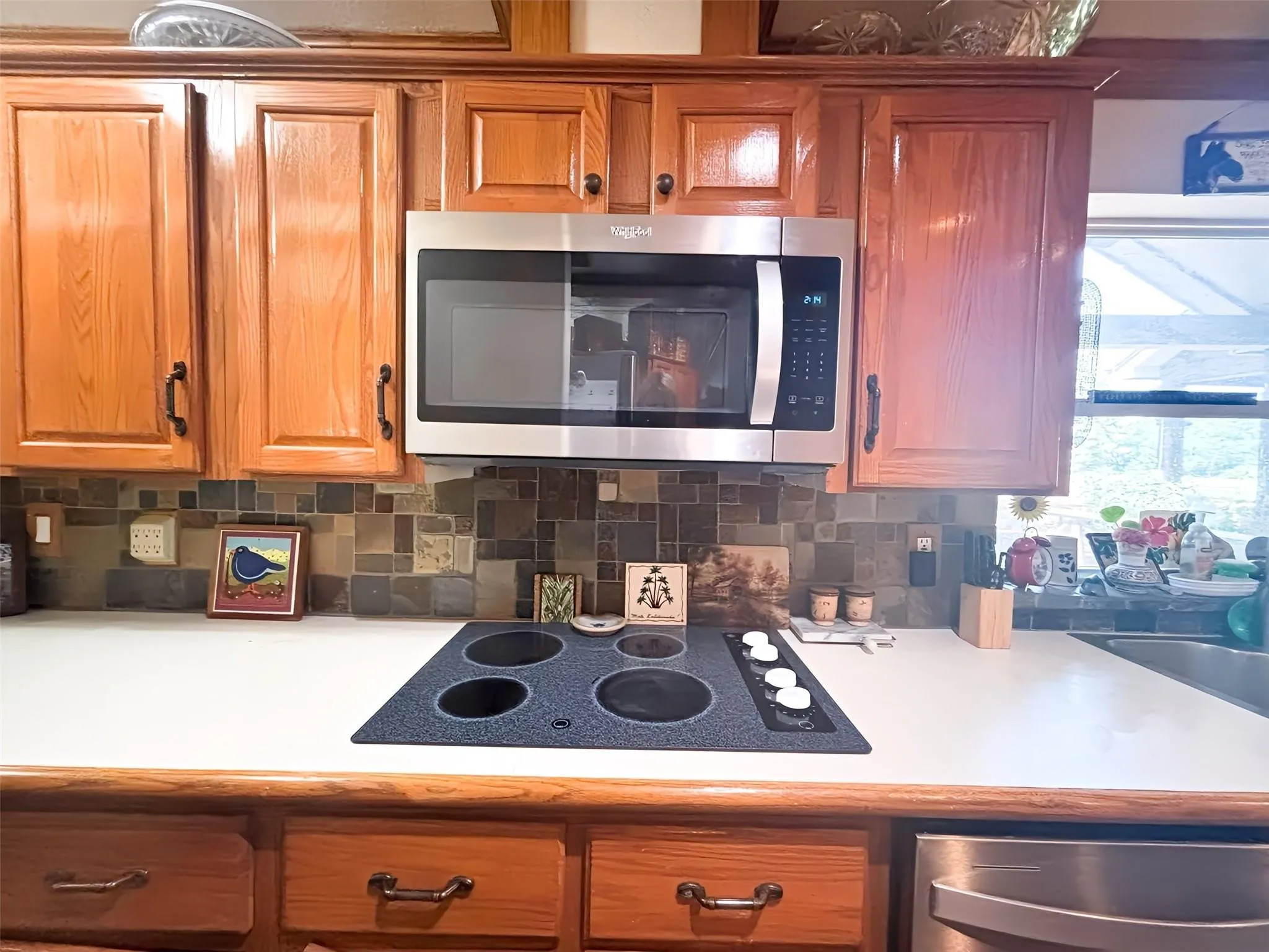 Kitchen featuring wood cabinetry, stainless steel microwave, integrated electric cooktop, and a mosaic tile backsplash