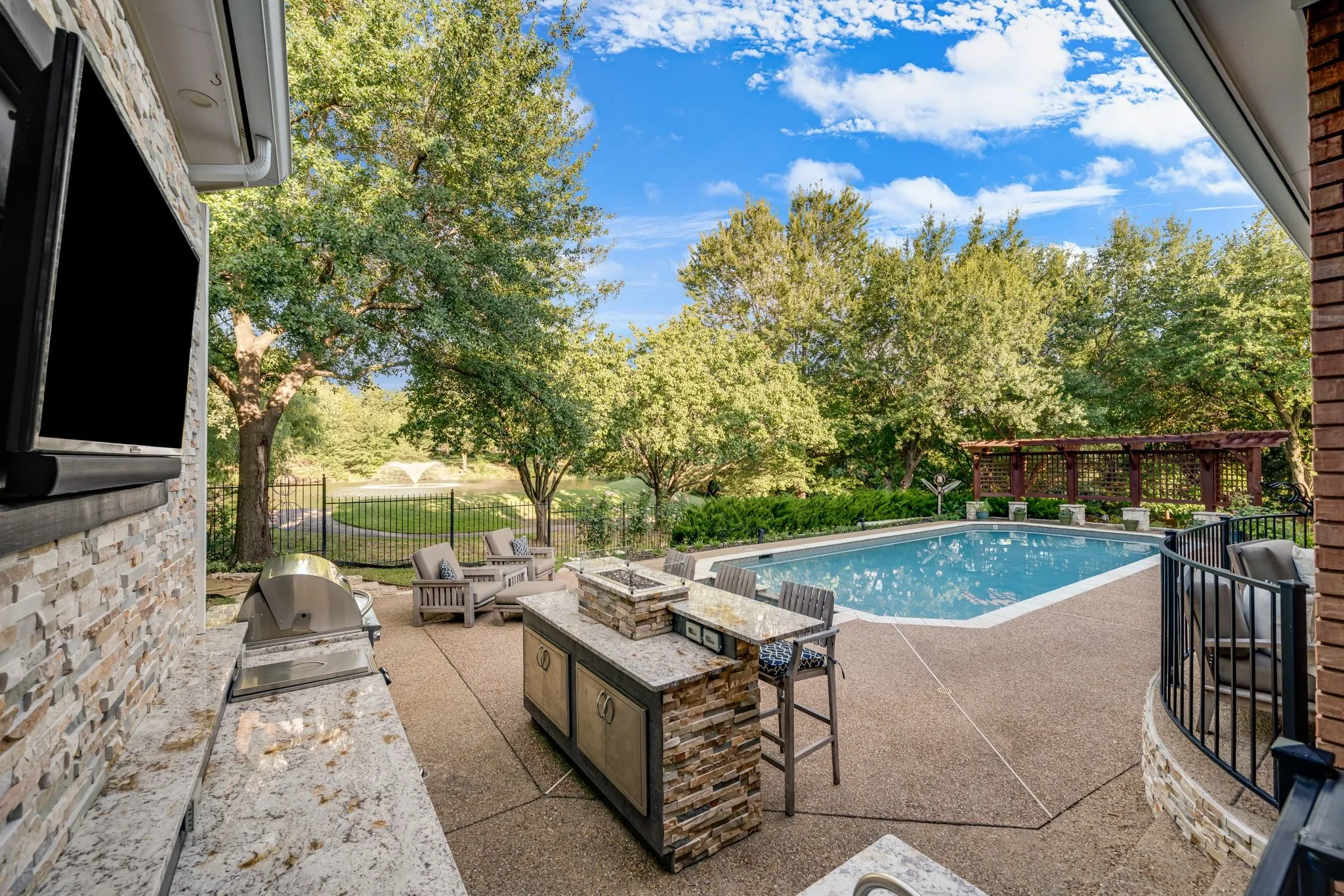 Expansive outdoor living area featuring a rectangular pool, a built-in outdoor kitchen with granite countertops, and multiple seating areas