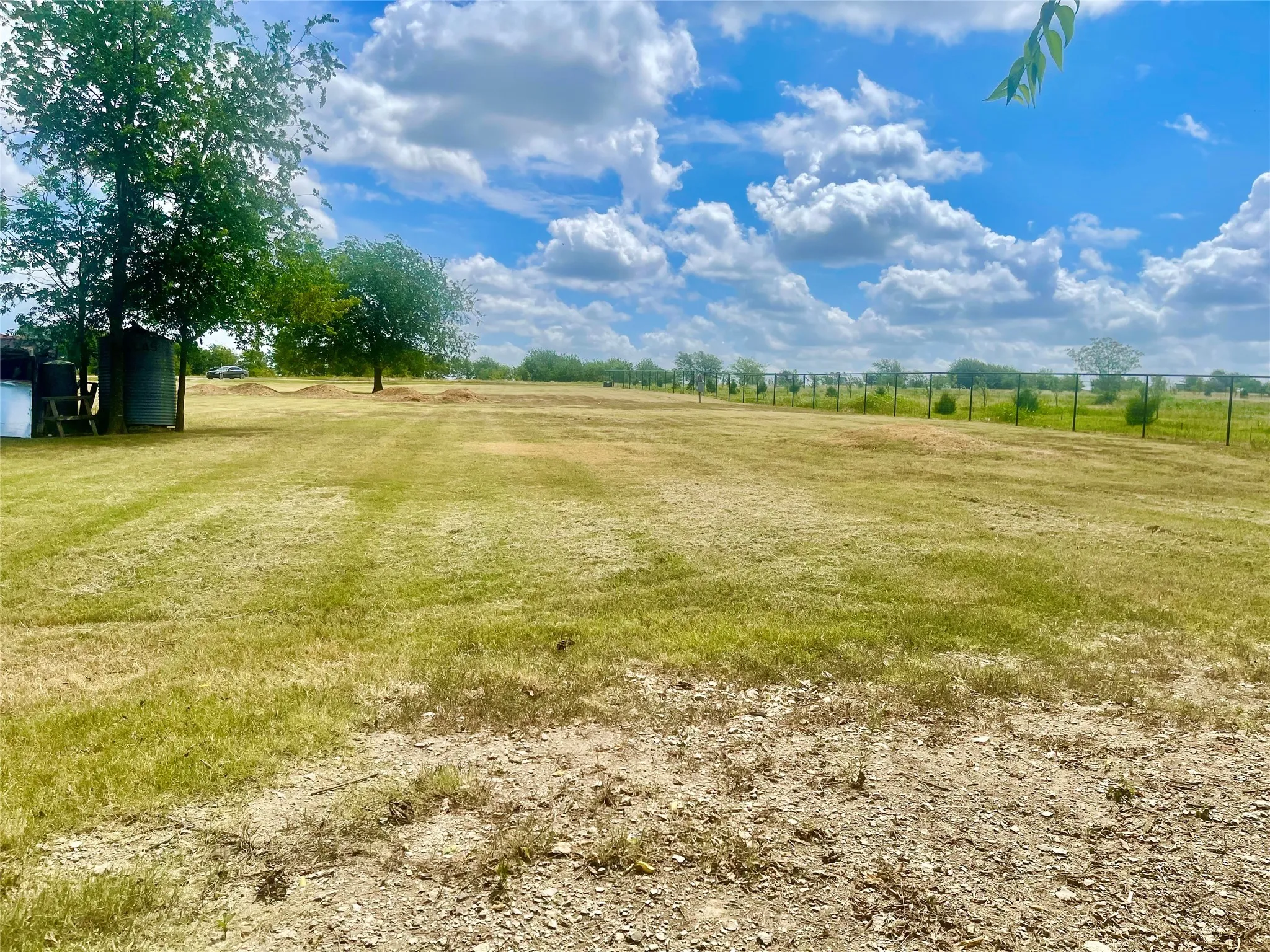Expansive grassy lot with mature trees, established fencing, and clear skies
