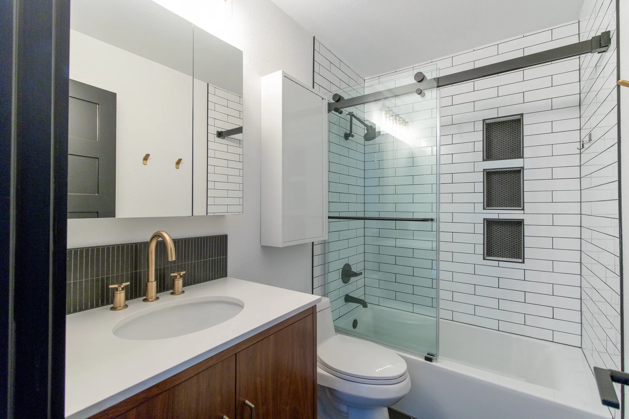 Bathroom featuring a wood-finish vanity with a white countertop and gold-tone faucet, a subway tile backsplash, and a medicine cabinet