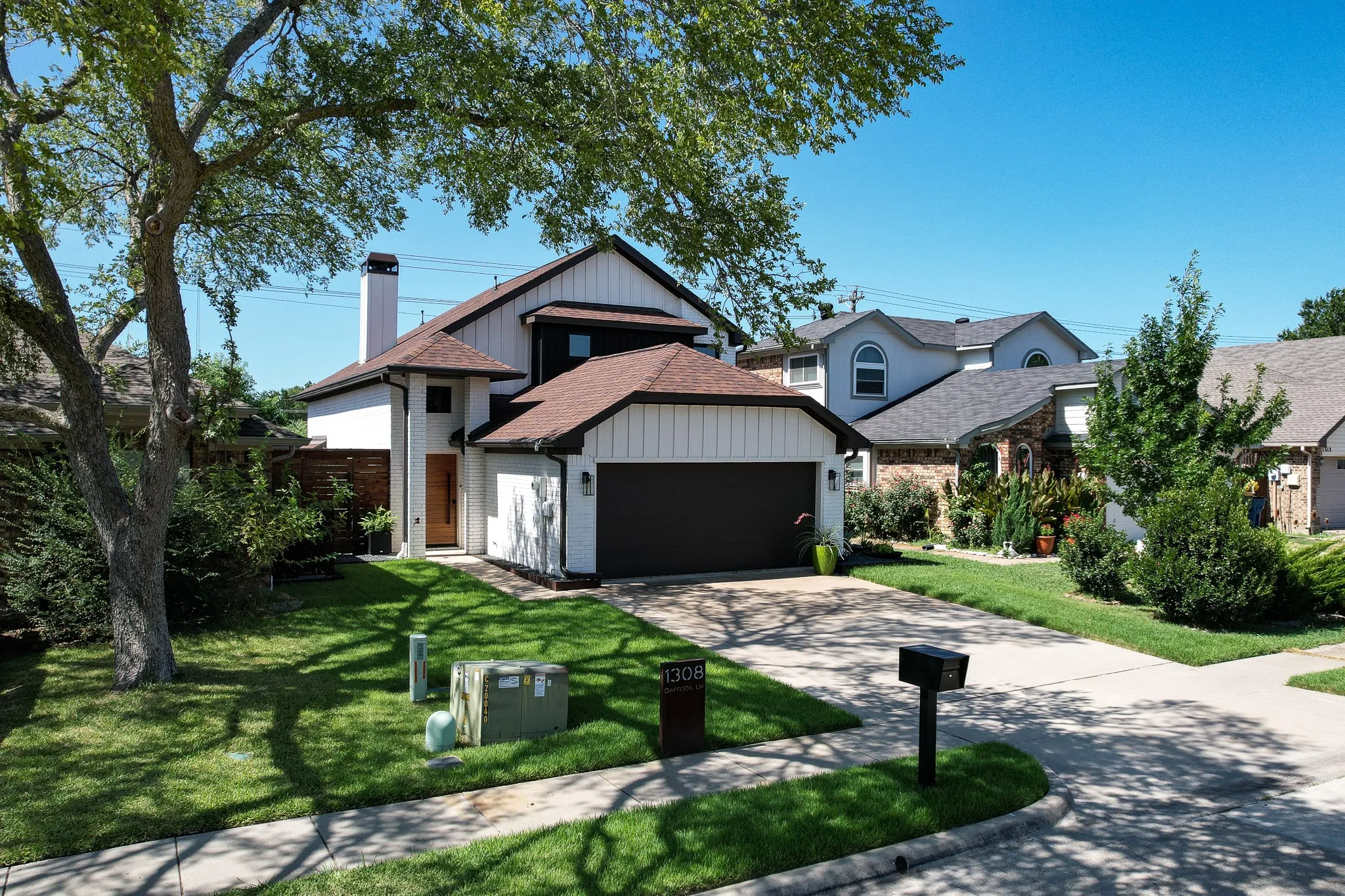 Modern exterior with a white and dark trim facade, an attached garage, a mature front yard tree, a paved driveway, and a shingle roof