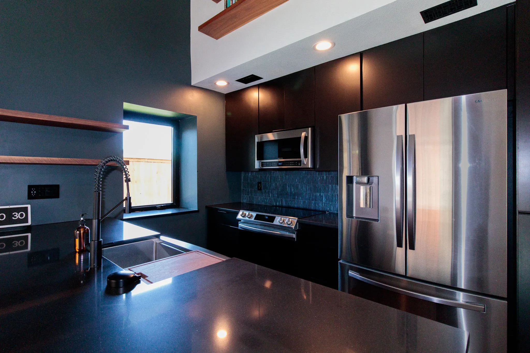 Sleek kitchen featuring dark cabinetry, stainless steel appliances, dark countertops, and a modern gooseneck faucet