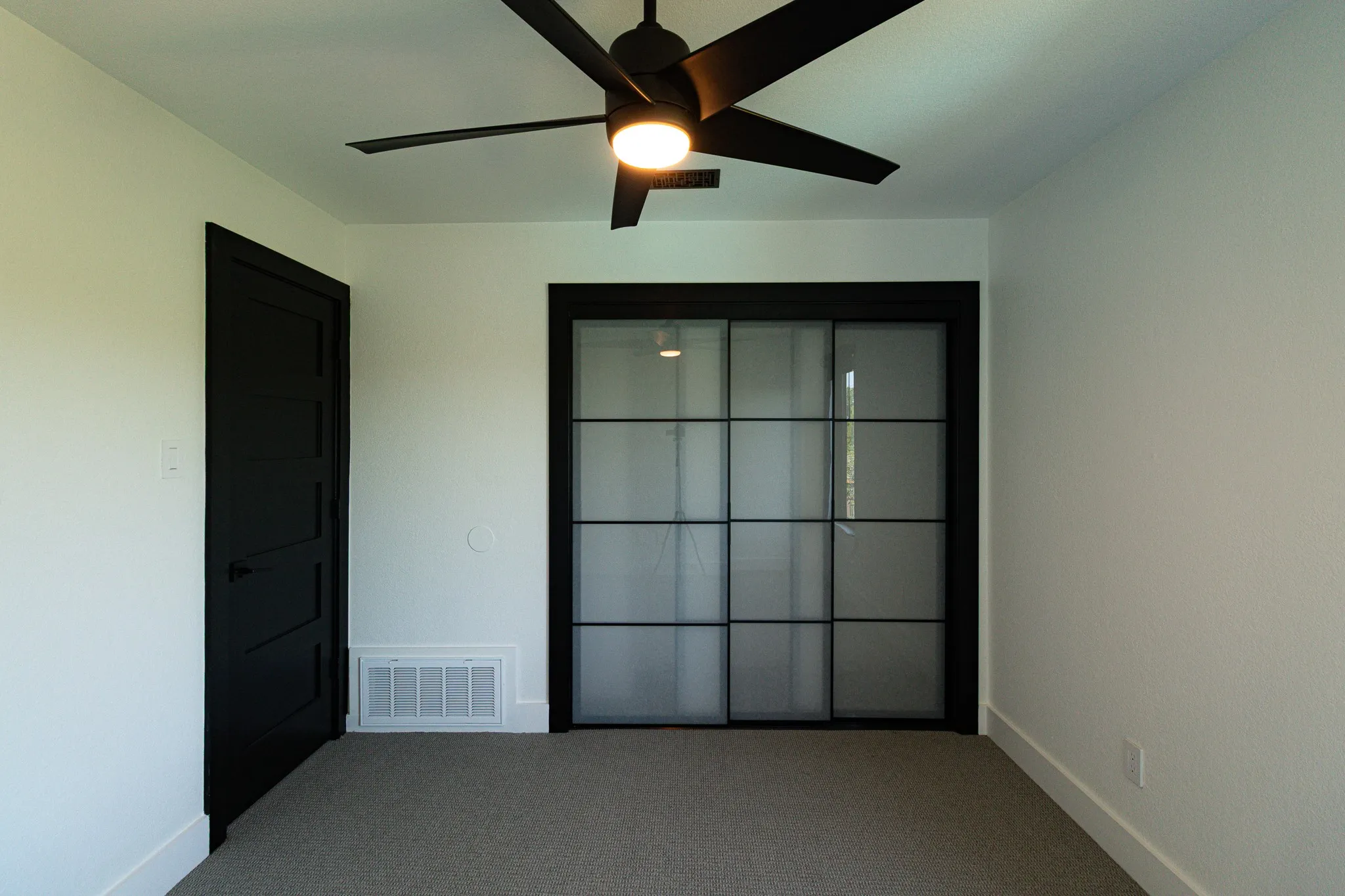 Contemporary bedroom featuring a black five-panel door, modern ceiling fan with integrated lighting, and a sliding glass door with black grid detailing
