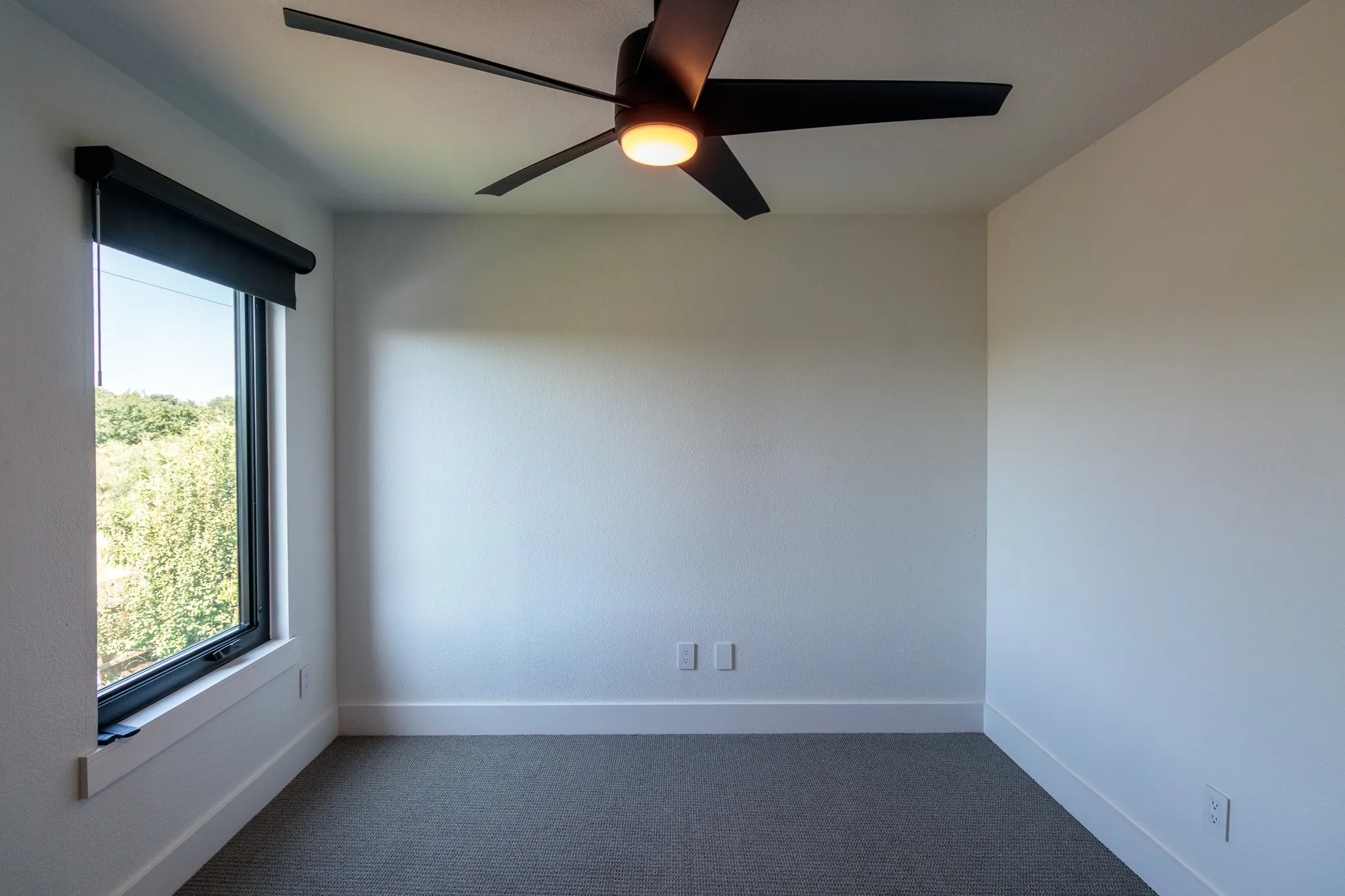 Neutral wall paint with baseboard trim, large window with roller shade, and modern ceiling fan with integrated lighting