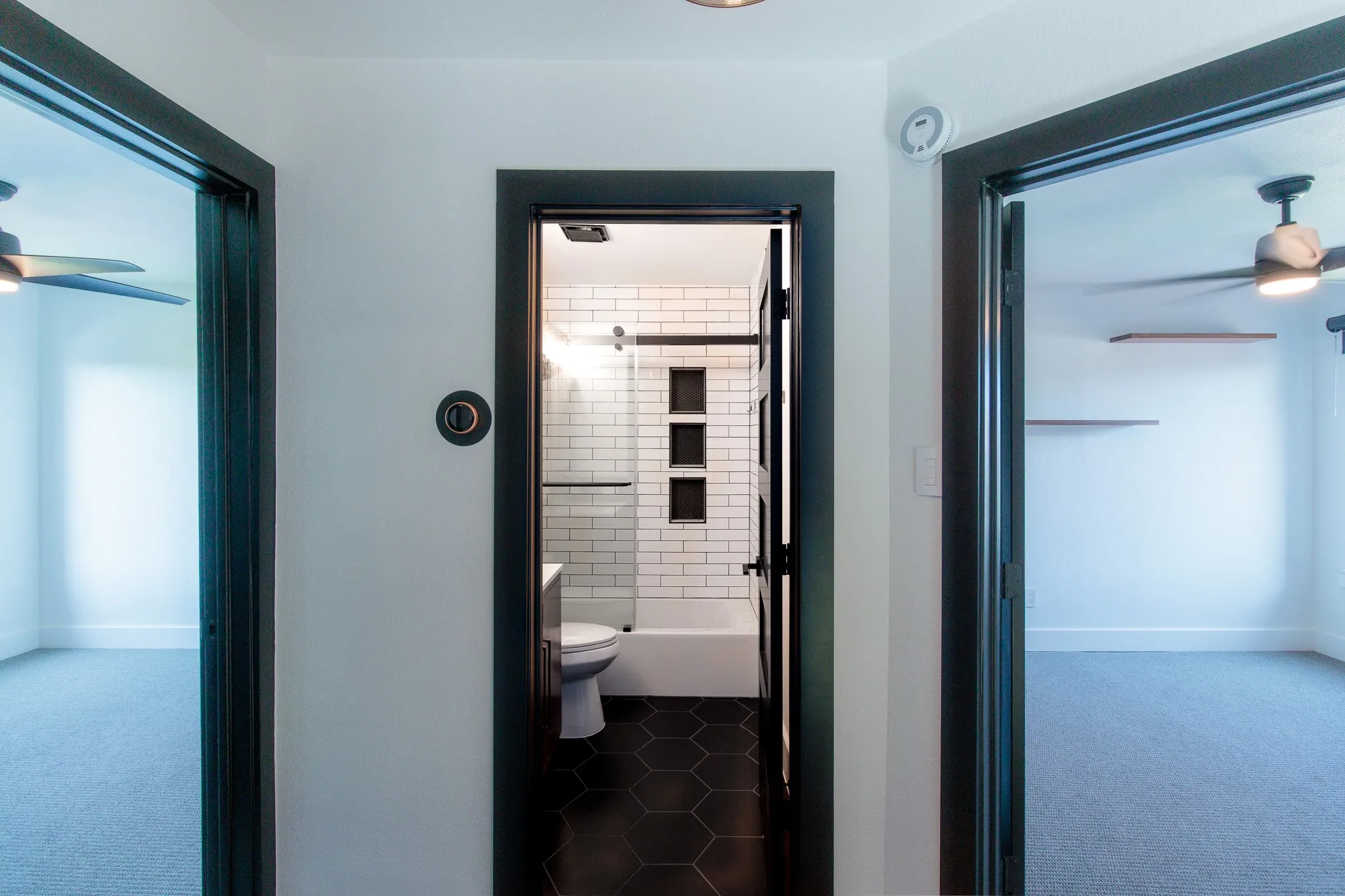 Modern bathroom featuring black hexagon tile flooring, a white subway tile shower surround with built-in niches, and a frameless glass shower door