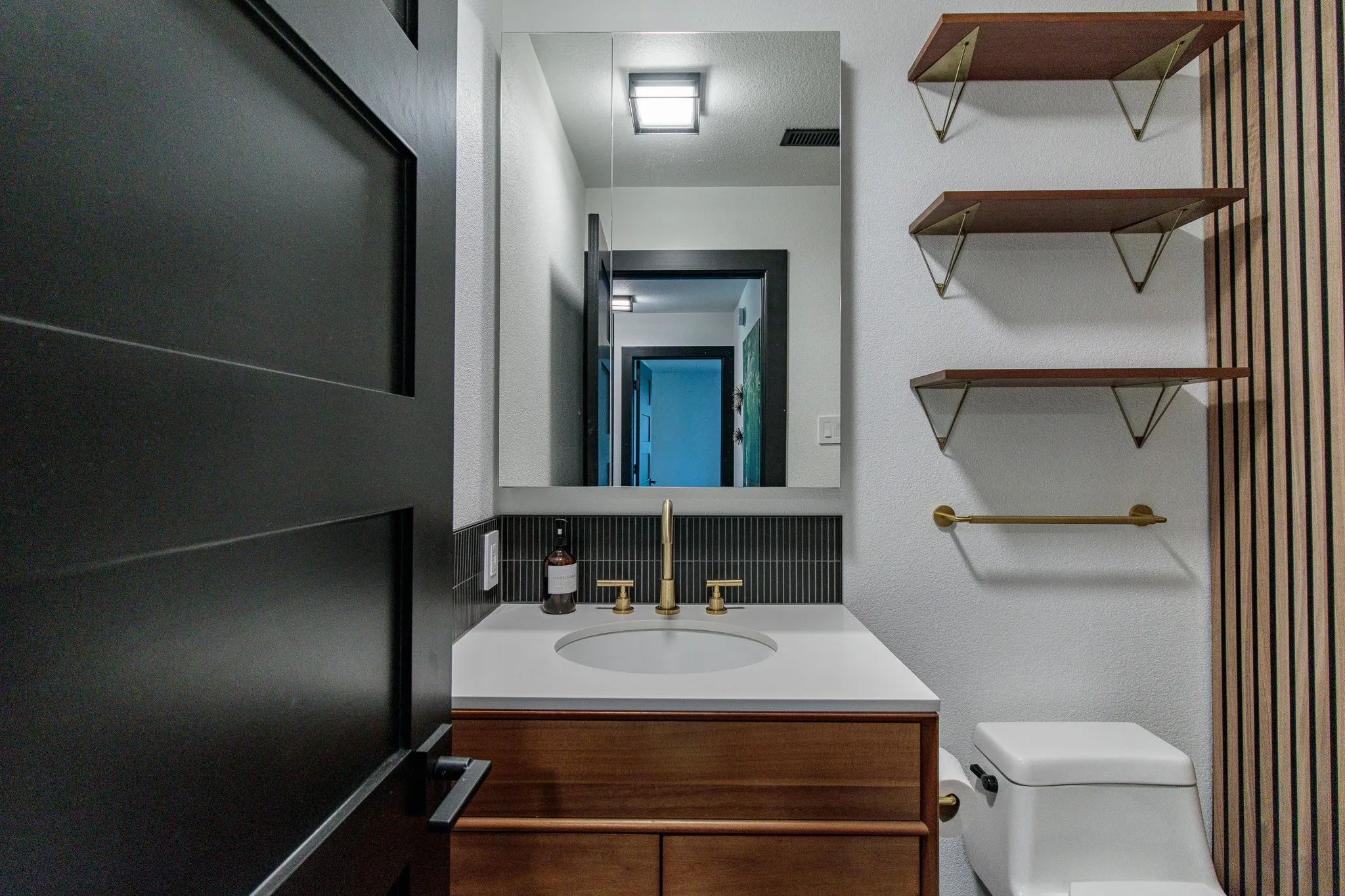 Modern bathroom featuring a wood-finish vanity with an integrated sink, brass fixtures, and a sleek rectangular mirror