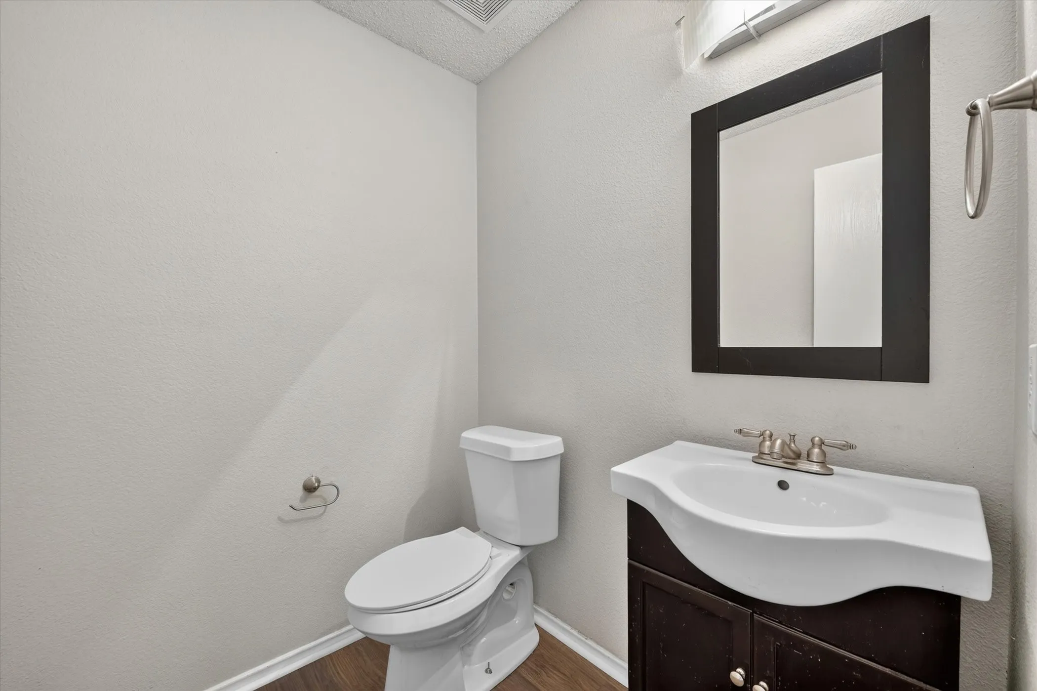 Powder room featuring a dark wood-finish vanity with an integrated white sink, framed mirror, and wood-finish flooring