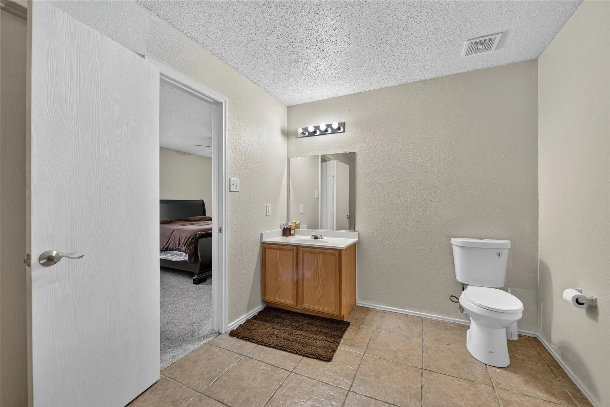 Bathroom featuring tile flooring, a wood-finish vanity with a white countertop, a mirror, and a wall-mounted light fixture