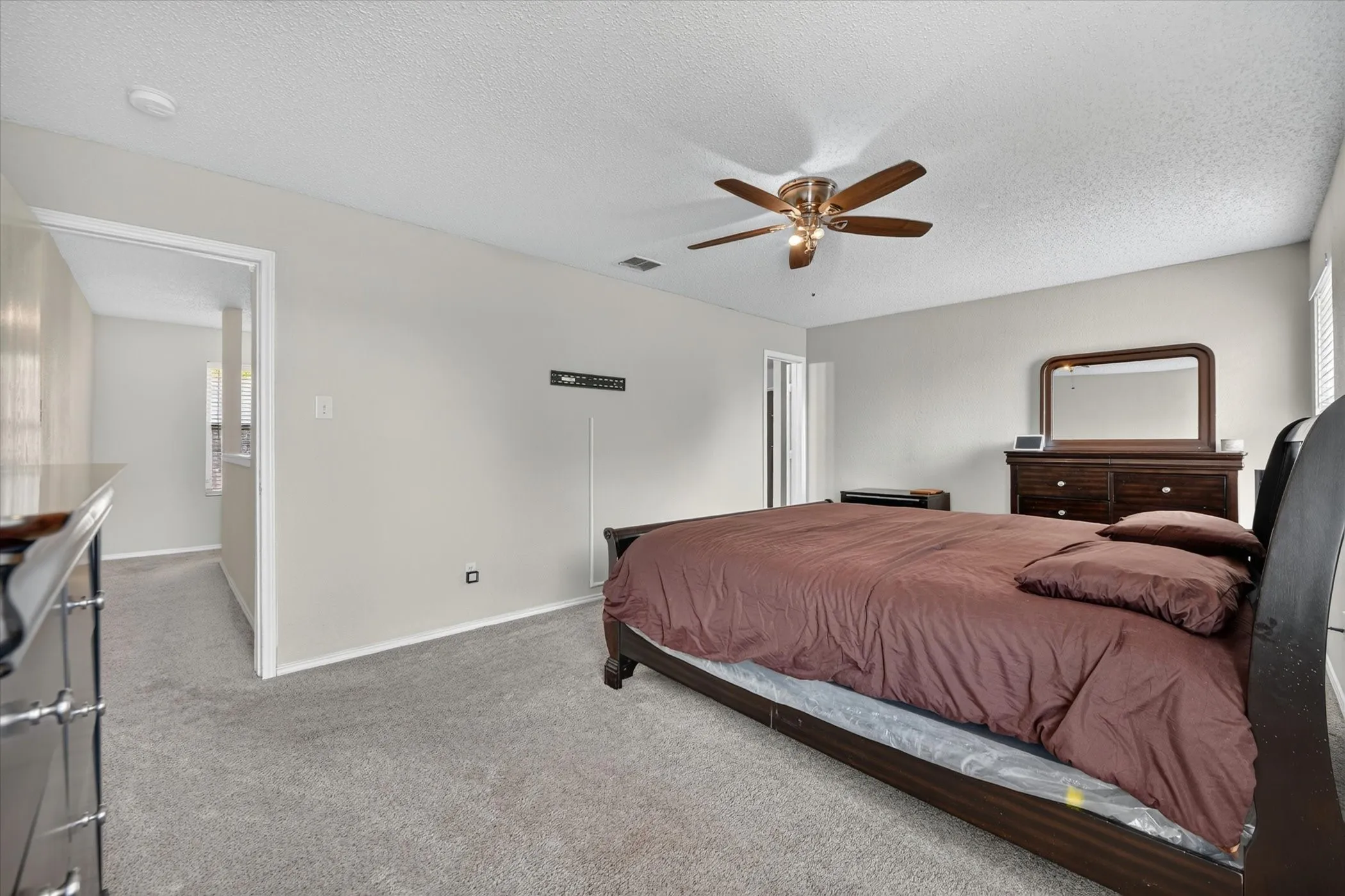 Spacious bedroom featuring light neutral wall tones, gray carpeting, a multi-speed ceiling fan, and white trim
