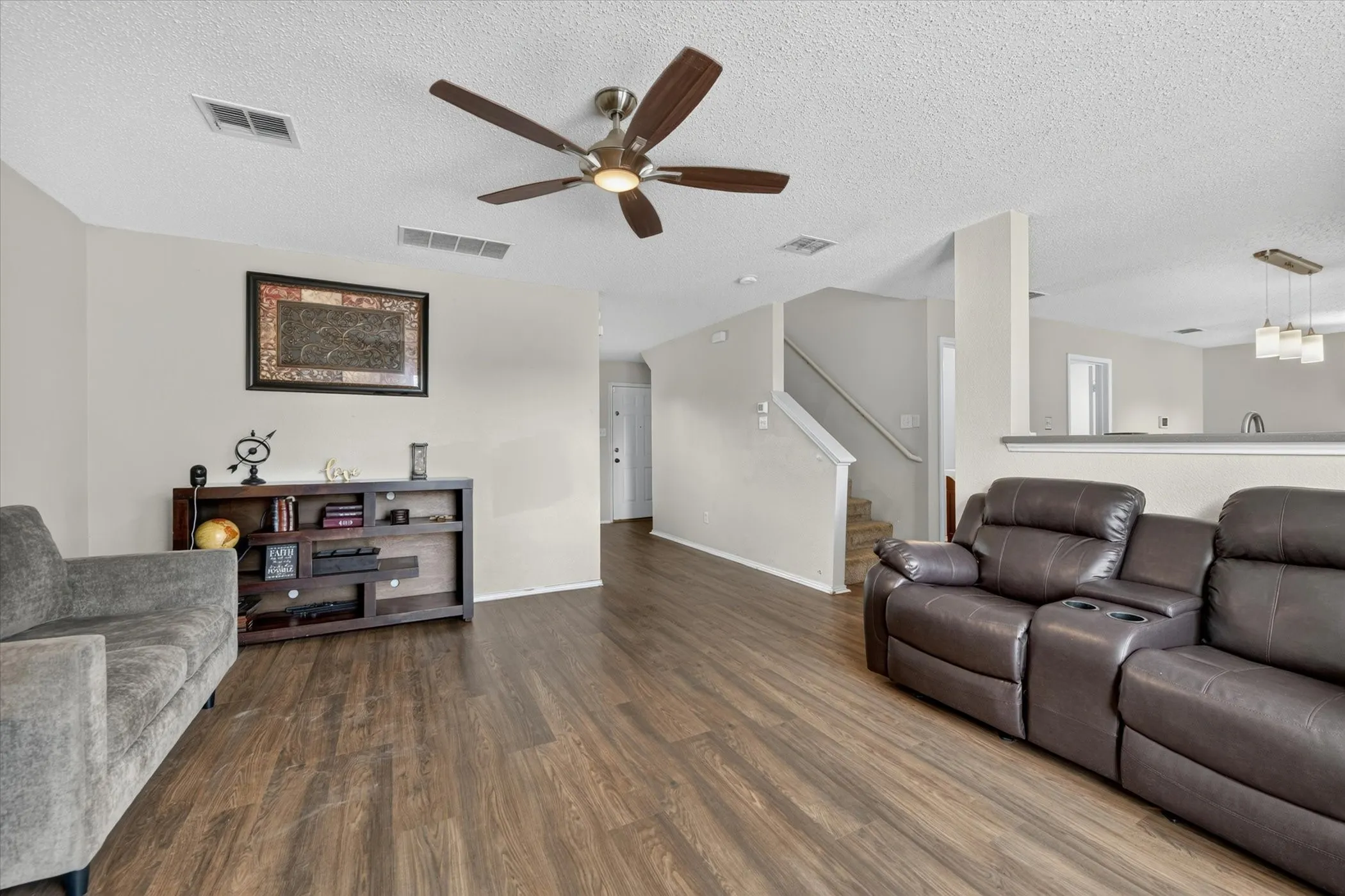 Spacious living area featuring wood-finish flooring, a ceiling fan with integrated lighting, and neutral wall tones