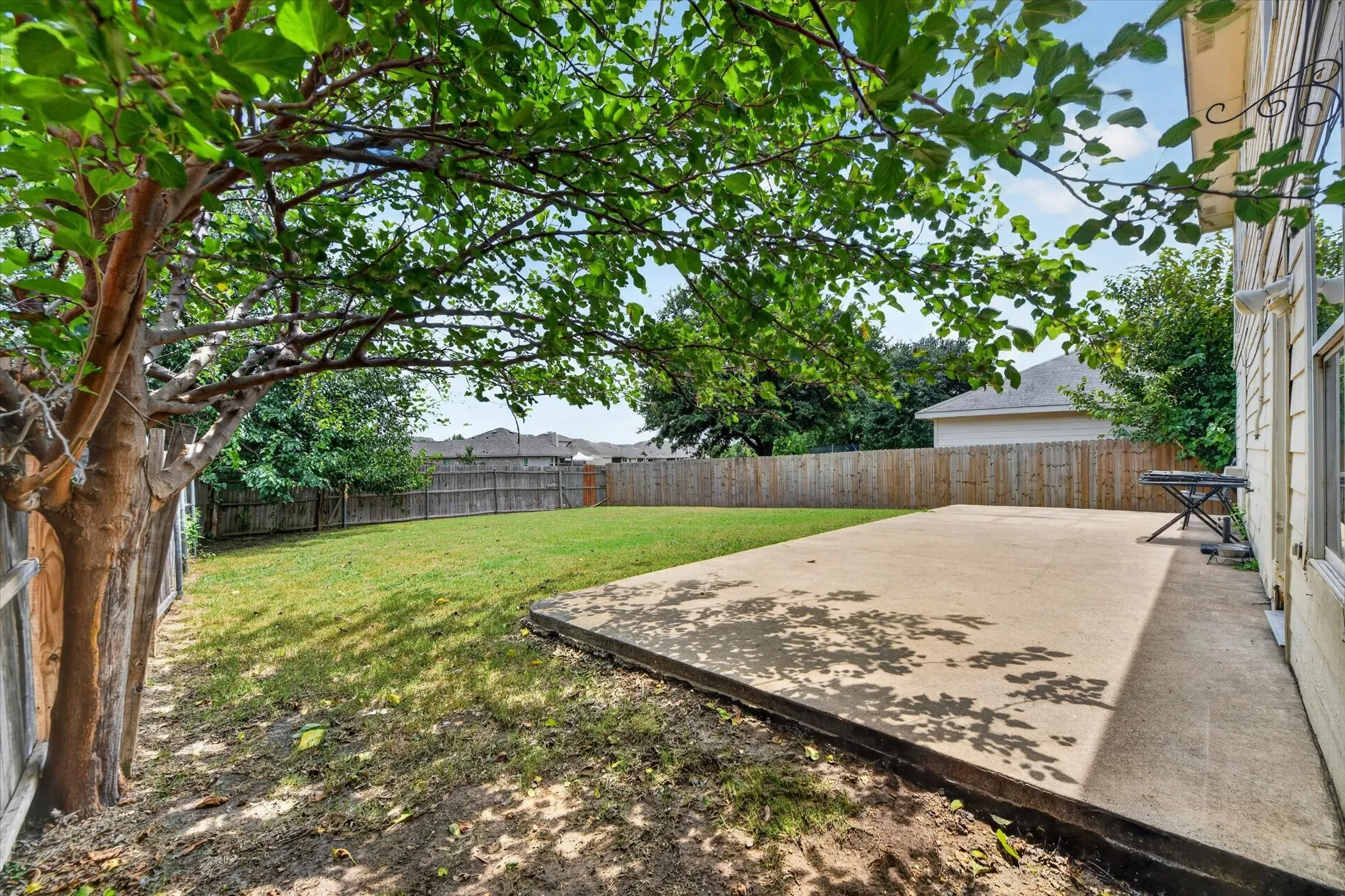 Spacious backyard featuring a large concrete patio, expansive lawn, and mature trees providing natural shade