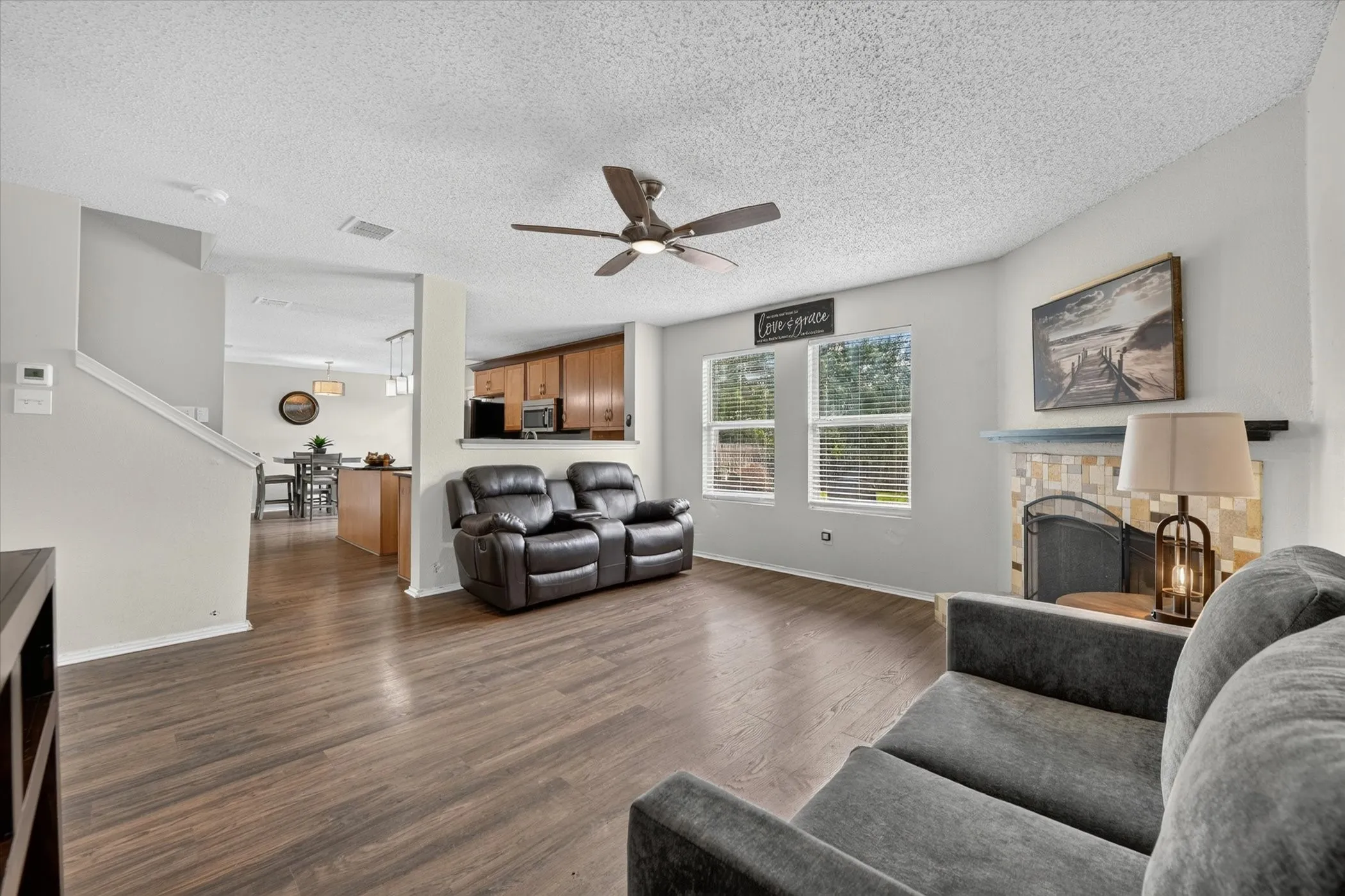 Living area featuring wood-finish flooring, a ceiling fan, and a fireplace with a tile surround and mantel