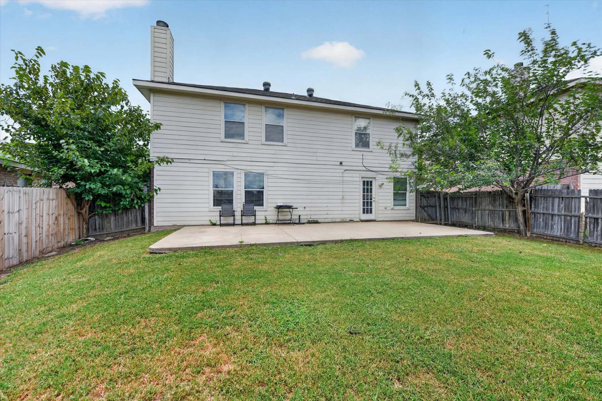 Expansive backyard featuring a concrete patio, mature trees, and a full privacy fence