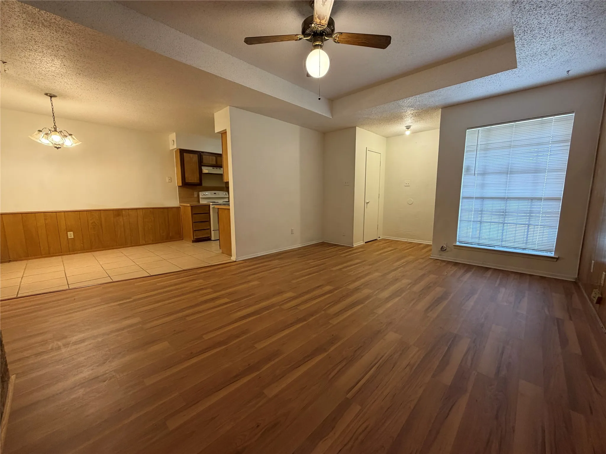 Open-concept living area featuring wood-finish flooring, a ceiling fan, and a large window with blinds
