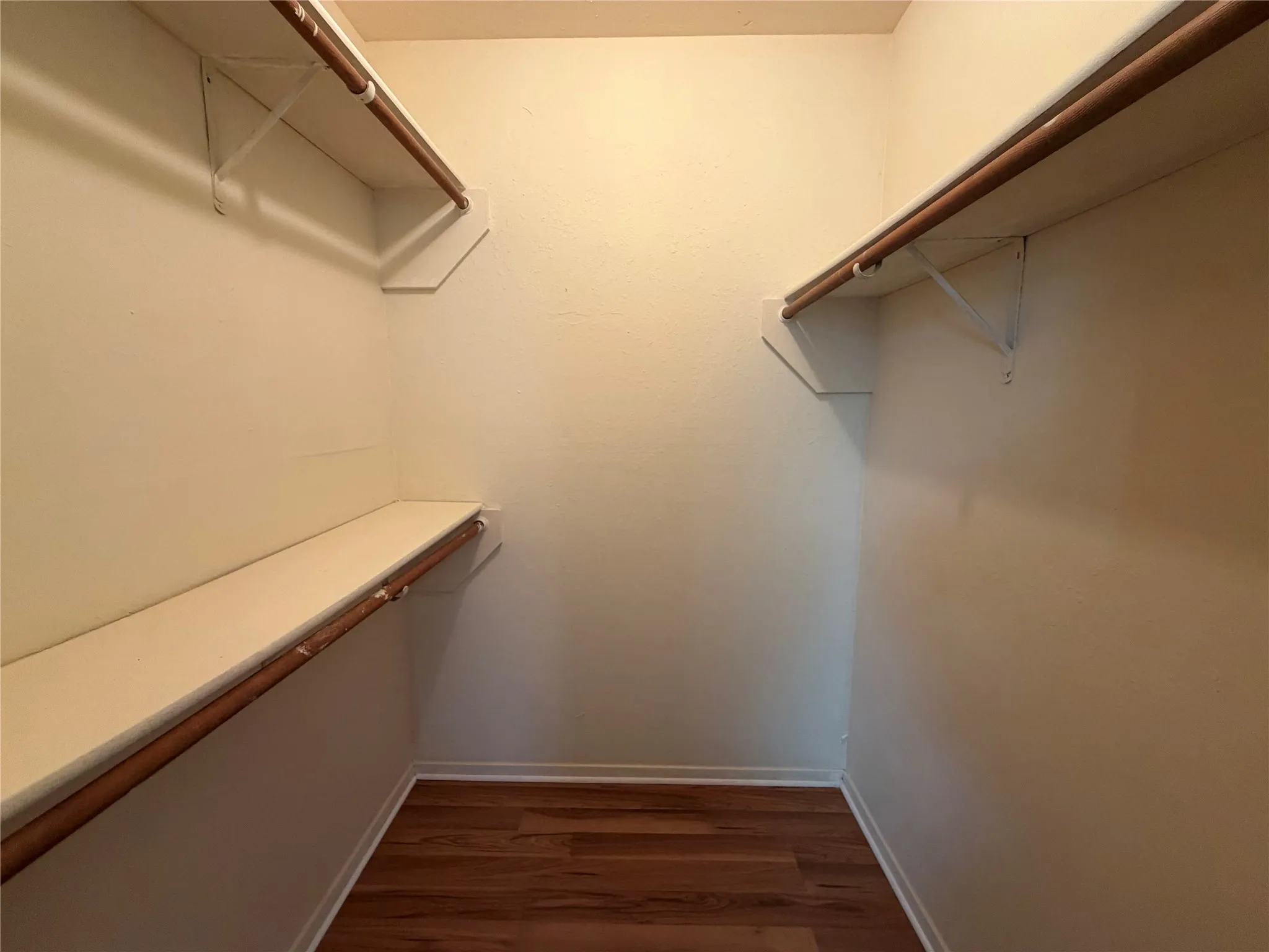 Walk-in closet featuring wood-finish flooring, light-toned walls, and built-in shelving with hanging rods on opposing sides