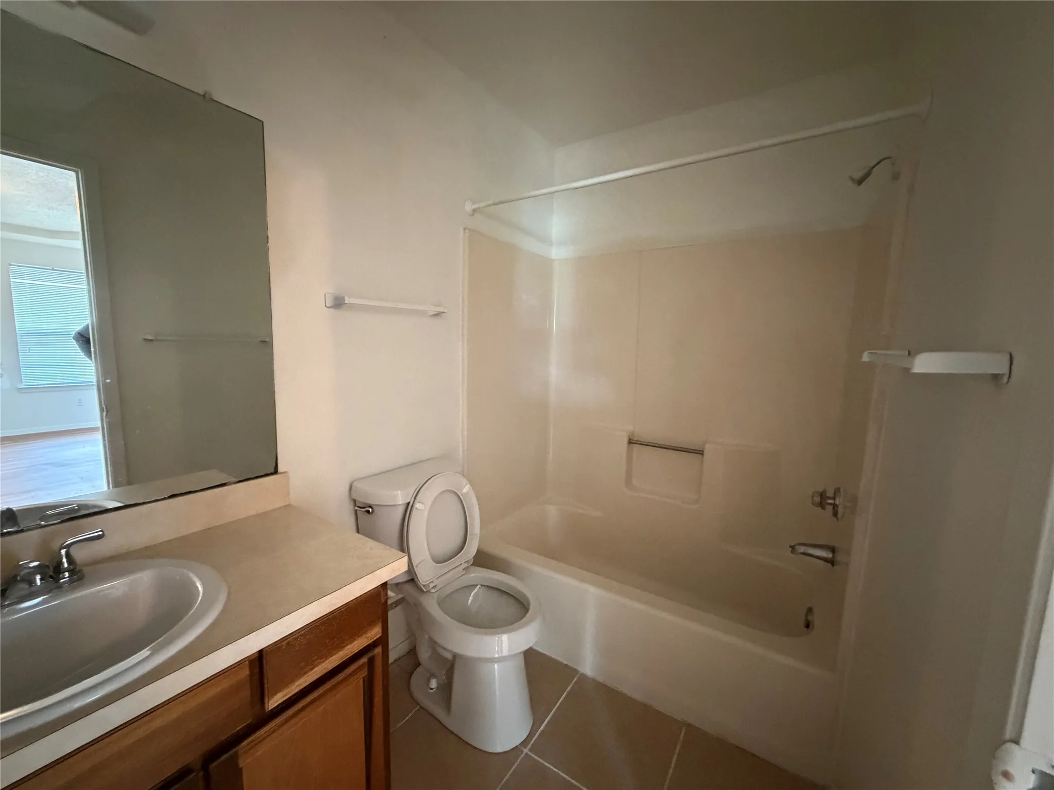 Full bathroom featuring a single vanity with wood-finish cabinetry, a rectangular mirror, a toilet, a bathtub with an integrated shower, and tile flooring