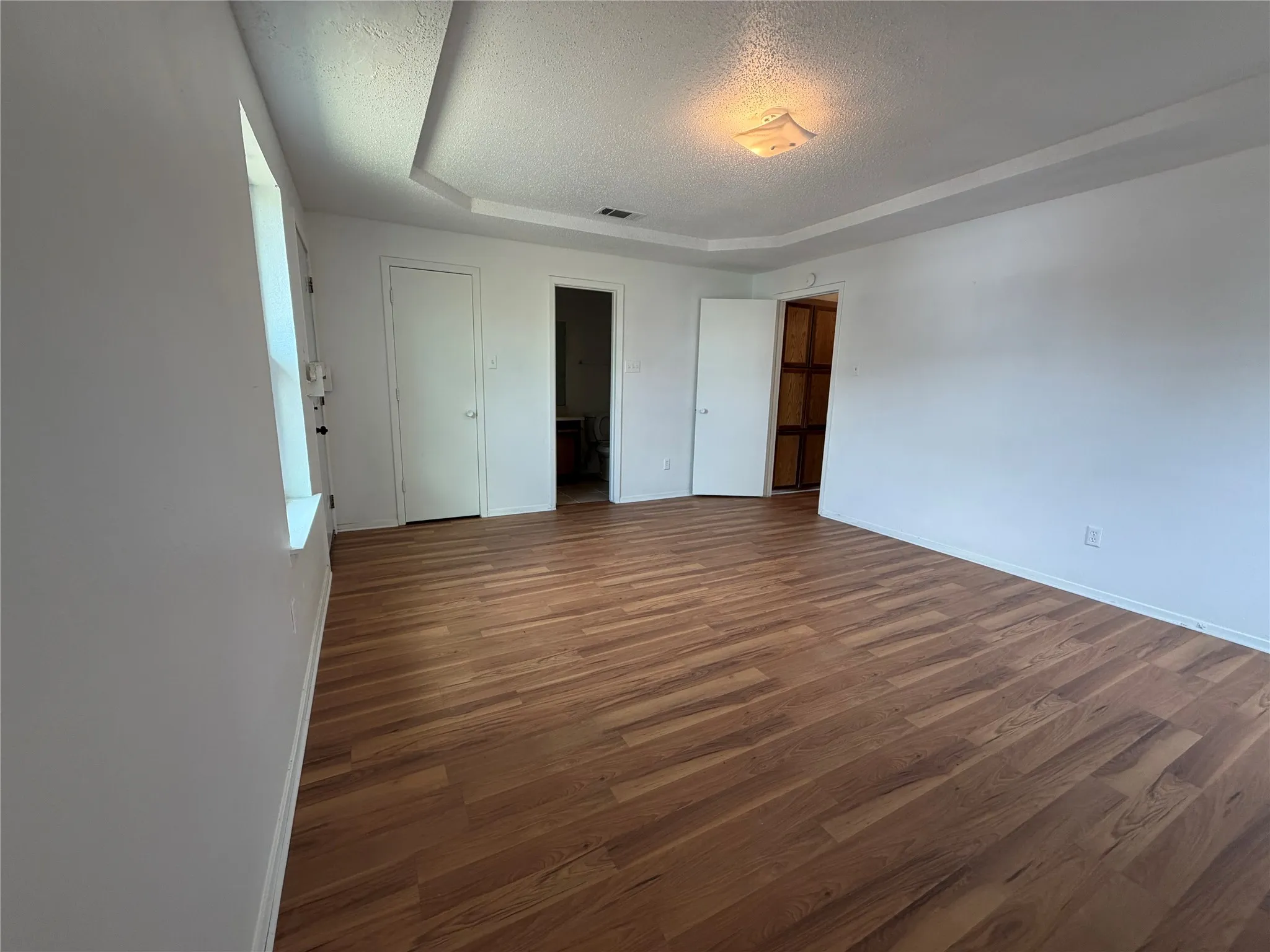 Spacious room featuring wood-finish flooring, white painted walls, a tray ceiling, and a flush mount lighting fixture