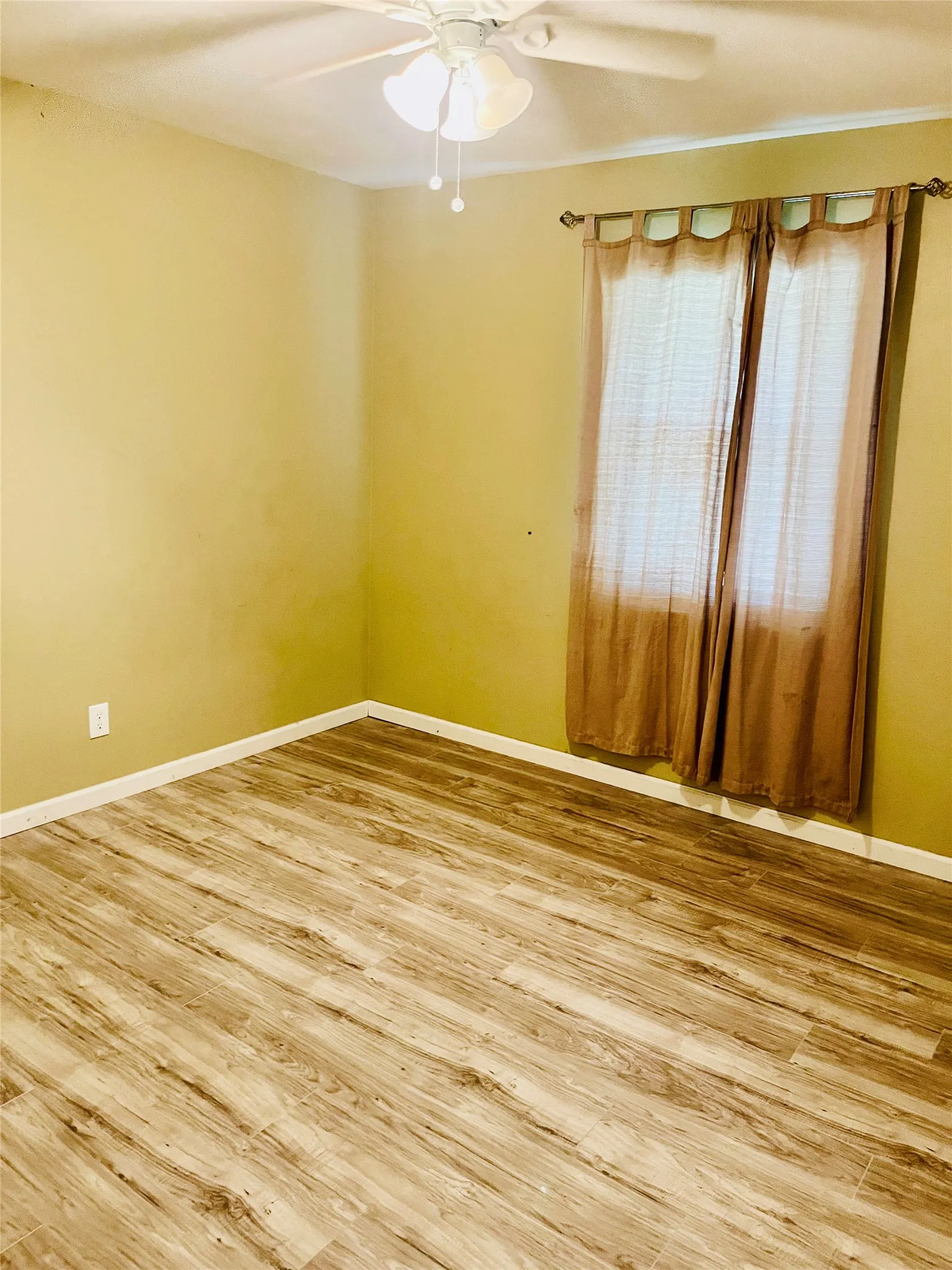 Room featuring wood-finish flooring, a ceiling fan, and window treatments on a single window