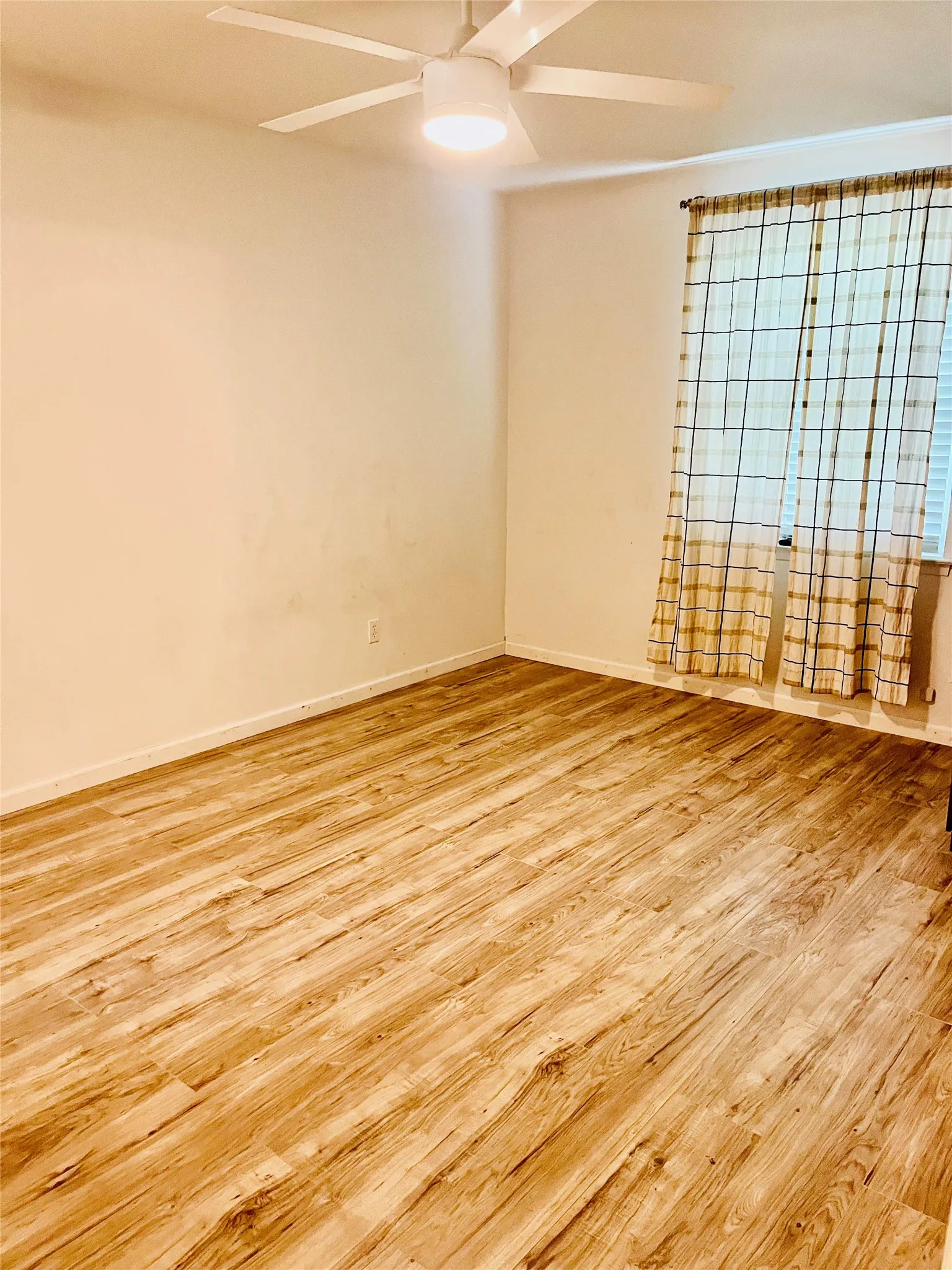 Spacious room featuring wood-finish flooring, a contemporary ceiling fan with integrated lighting, and a window with blinds