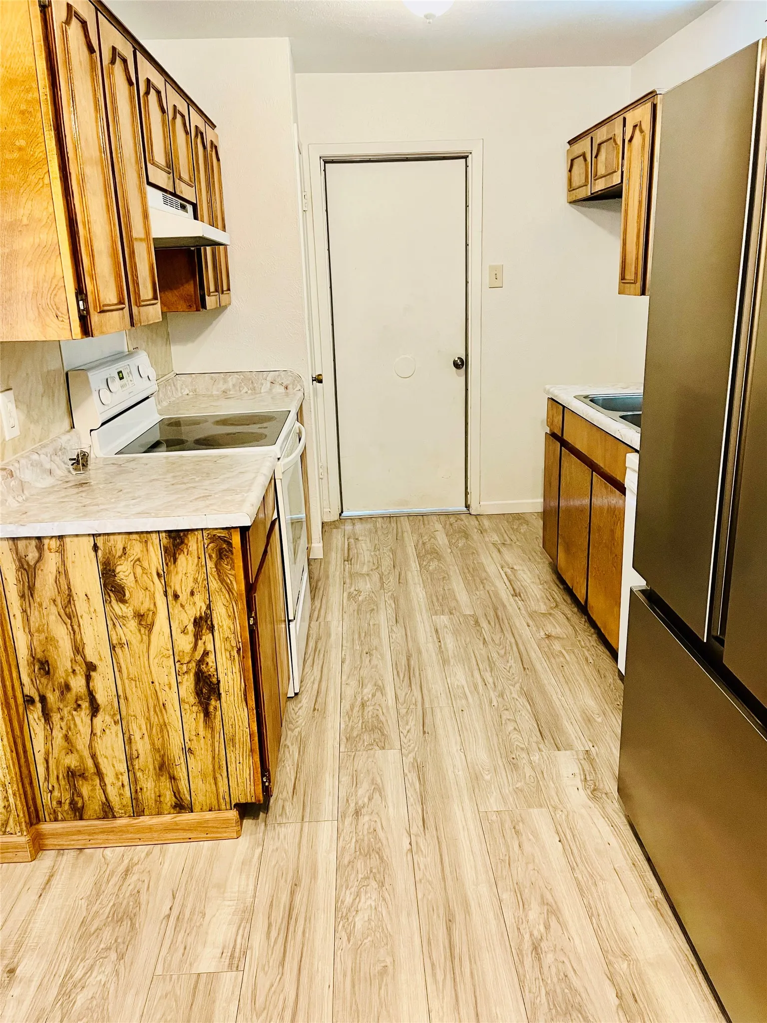 Galley kitchen featuring wood-finish cabinetry, light-toned countertops, and wood-look flooring