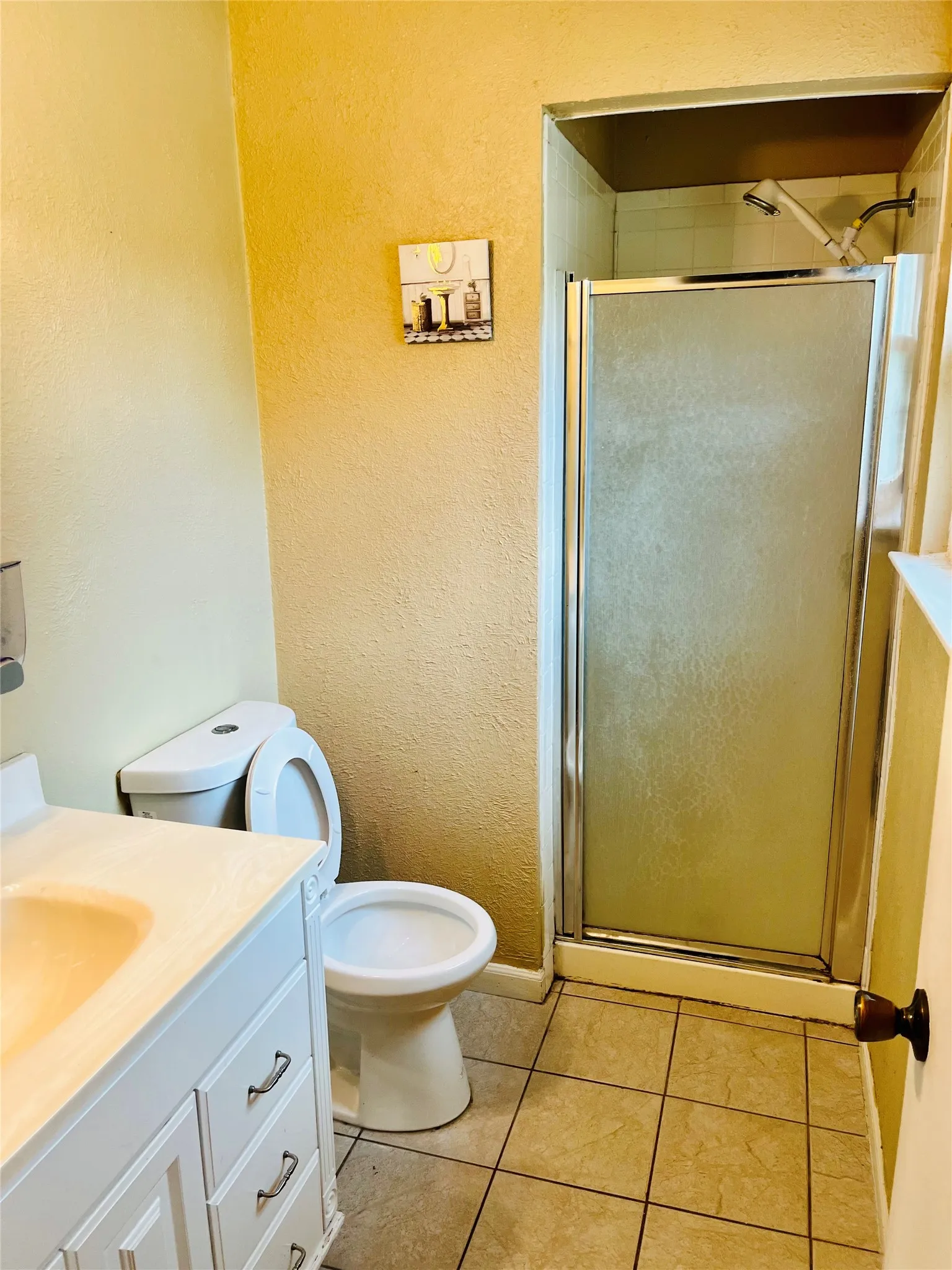 Bathroom featuring a shower stall with a framed glass door, white toilet, and a white vanity with integrated sink