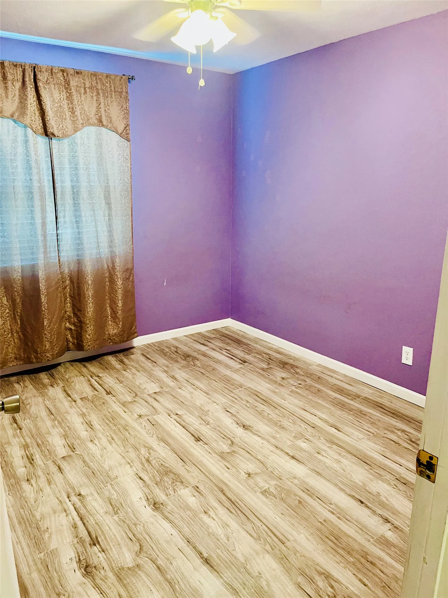 Room featuring wood-finish flooring, purple wall paint, and a ceiling fan with light fixture
