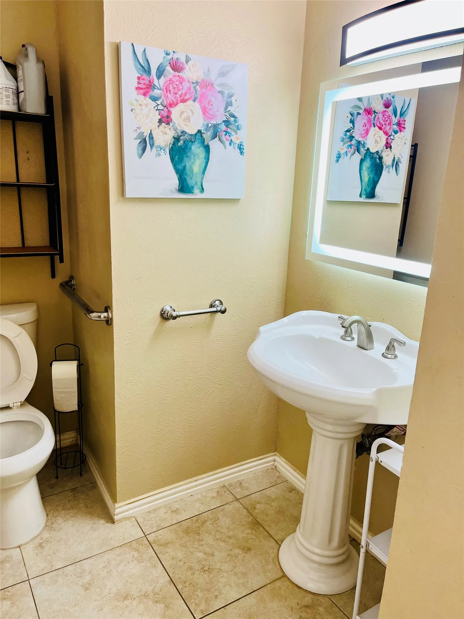 Pedestal sink with brushed nickel faucet, illuminated mirror, and tile flooring