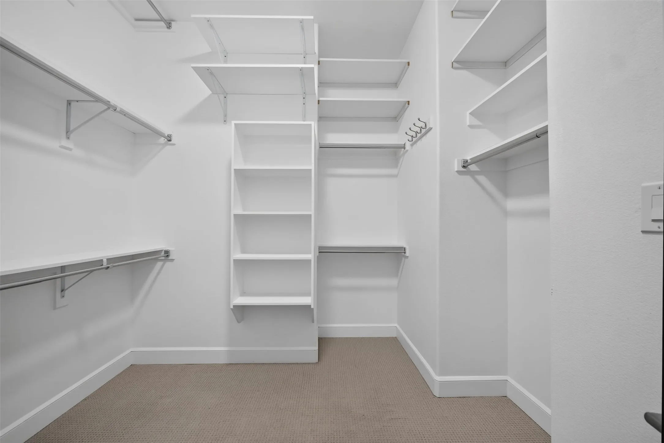 Spacious walk-in closet featuring white wall shelving, metal hanging rods, built-in cubbies, and neutral-toned carpeting