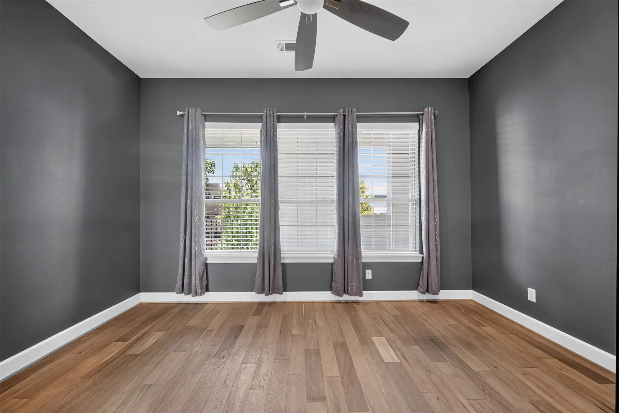 Room with wood-finish flooring, dark gray walls, and white baseboards
