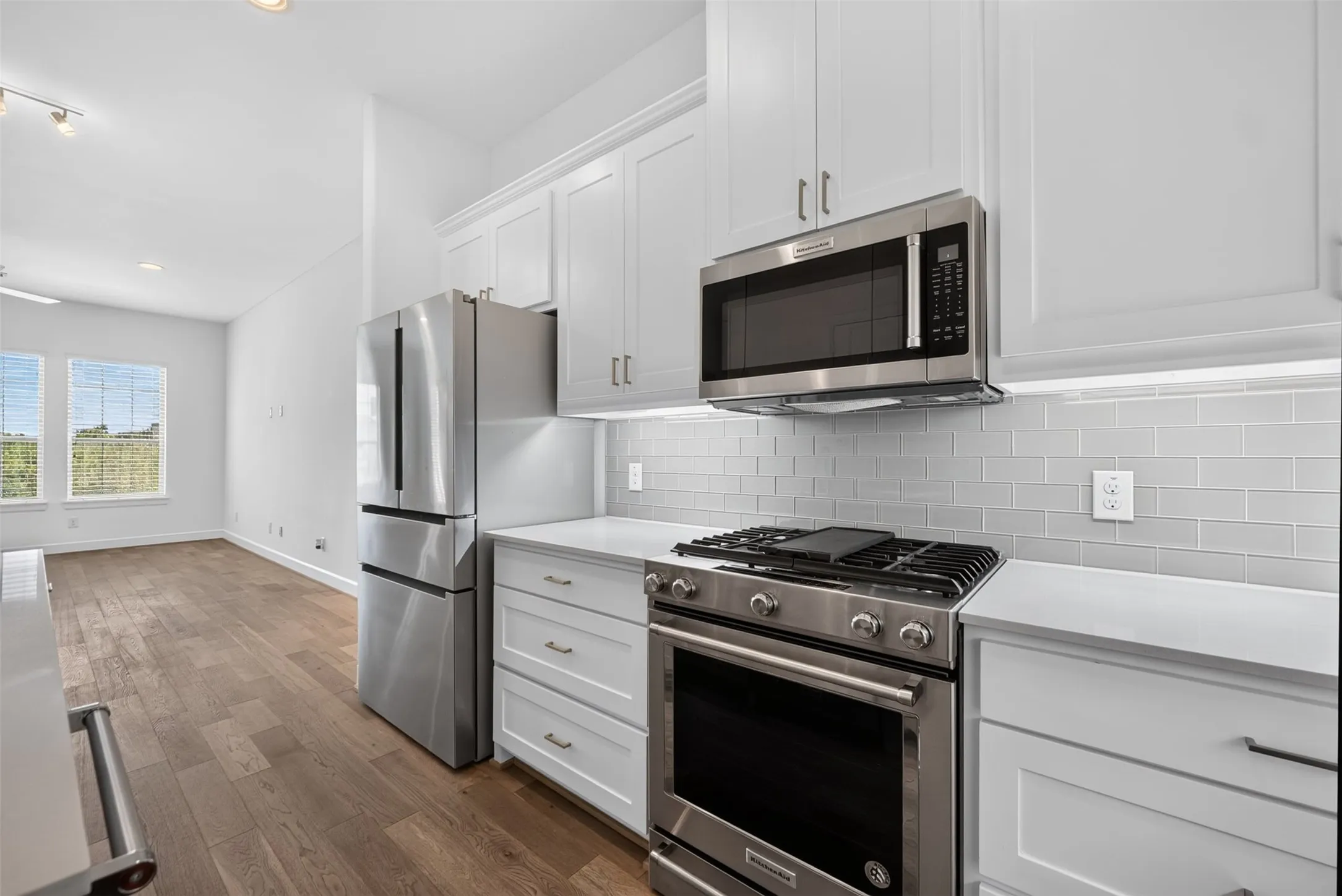 Modern kitchen featuring white shaker cabinetry, stainless steel appliances, light gray subway tile backsplash, and light-toned countertops