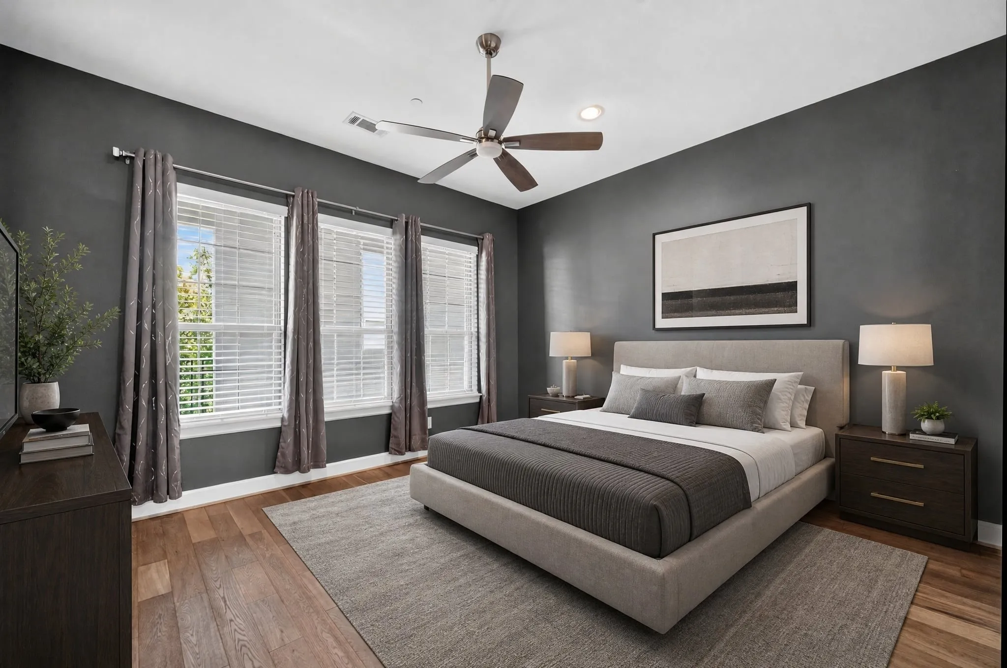 Spacious room featuring rich wood-finish flooring, dark accent walls, and three large windows