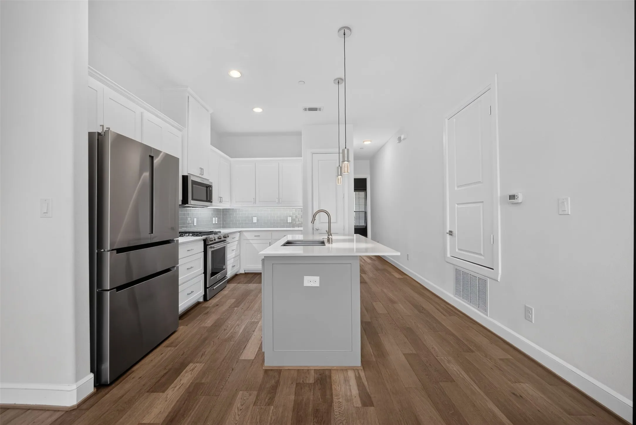 Modern kitchen featuring wood-finish flooring, white cabinetry, and stainless steel appliances