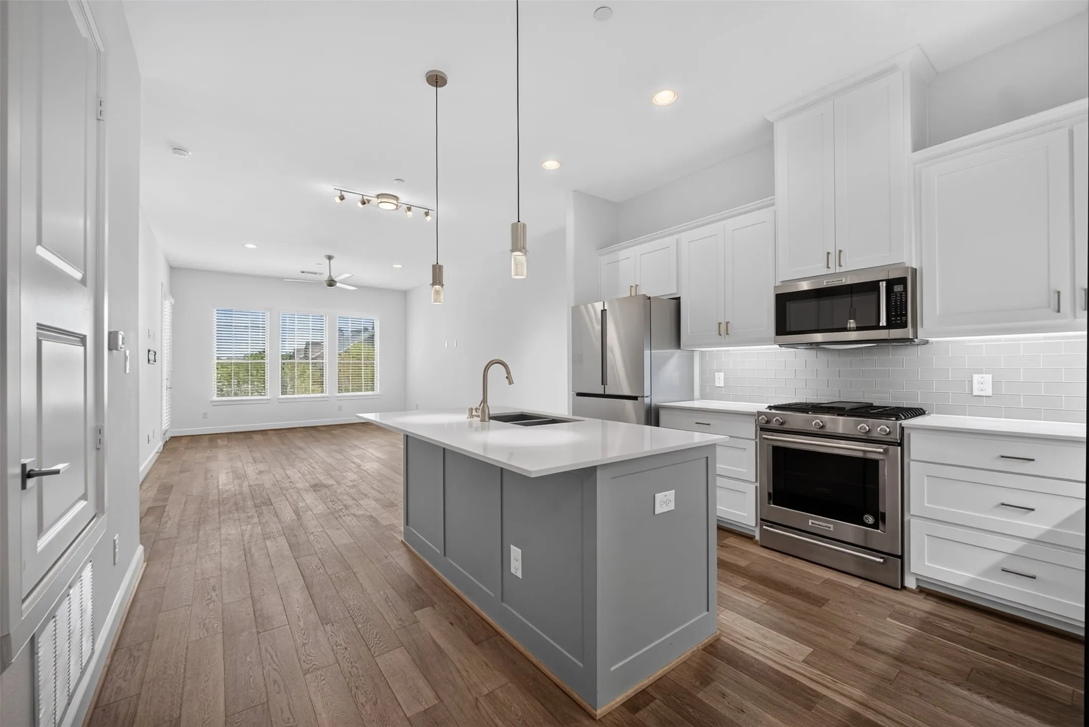 Open-concept kitchen and living area featuring stainless steel appliances, white shaker cabinetry, a subway tile backsplash, and wood-finish flooring