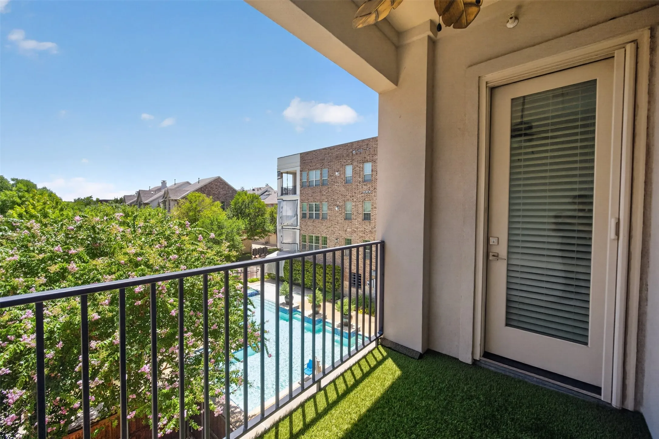 Private balcony featuring faux turf flooring, black metal railings, and an exterior door with integrated blinds