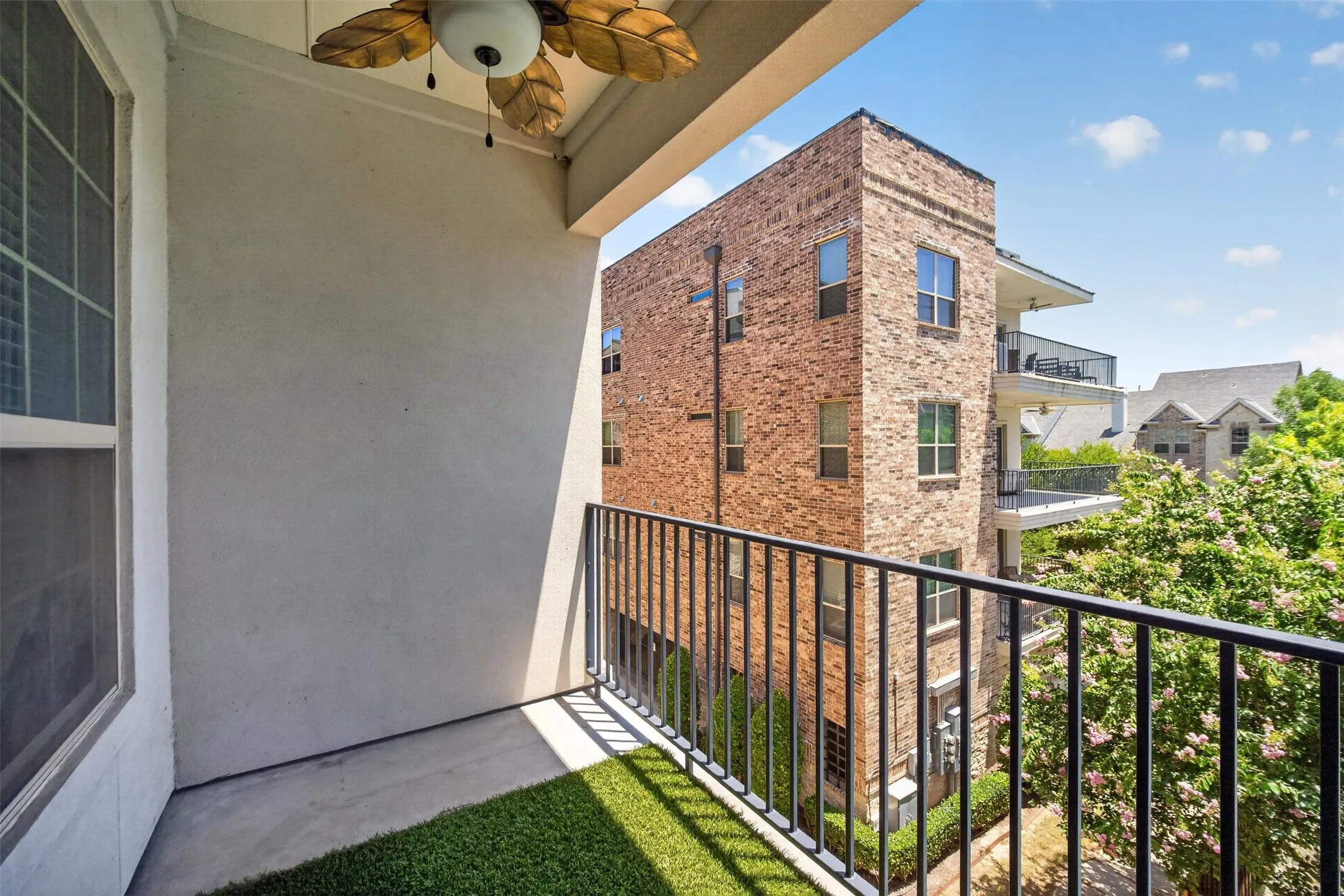 Private balcony featuring a ceiling fan with leaf-shaped blades, concrete flooring partially covered with artificial turf, and black metal railings