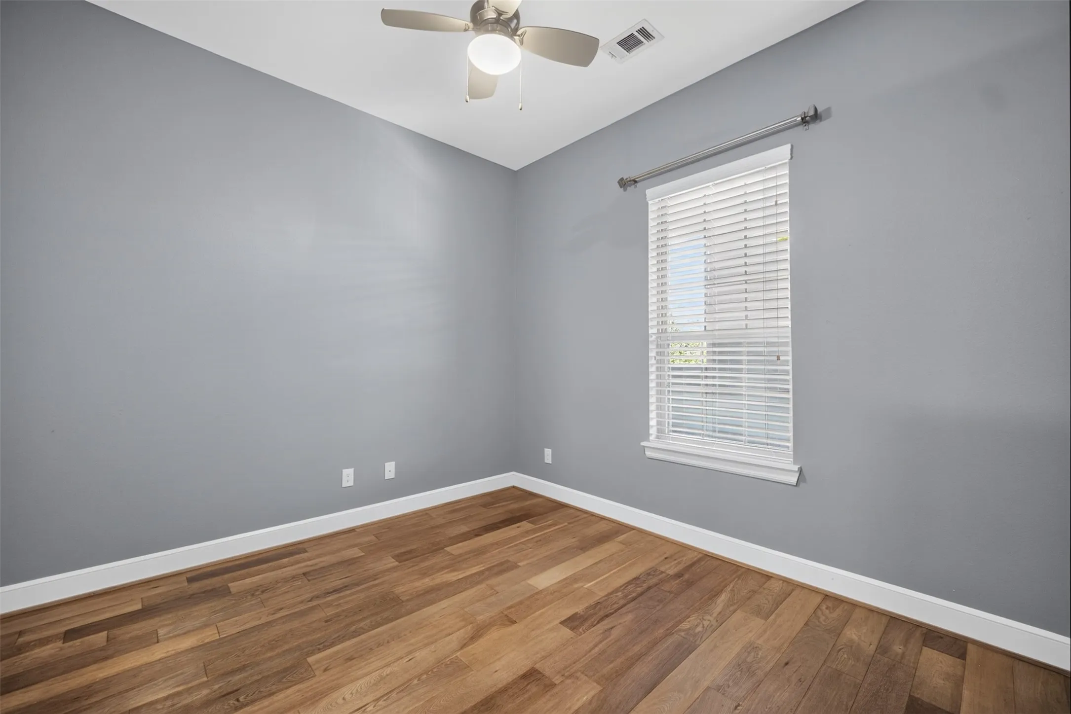 Room featuring wood-finish flooring, a ceiling fan with integrated lighting, and a single window with blinds