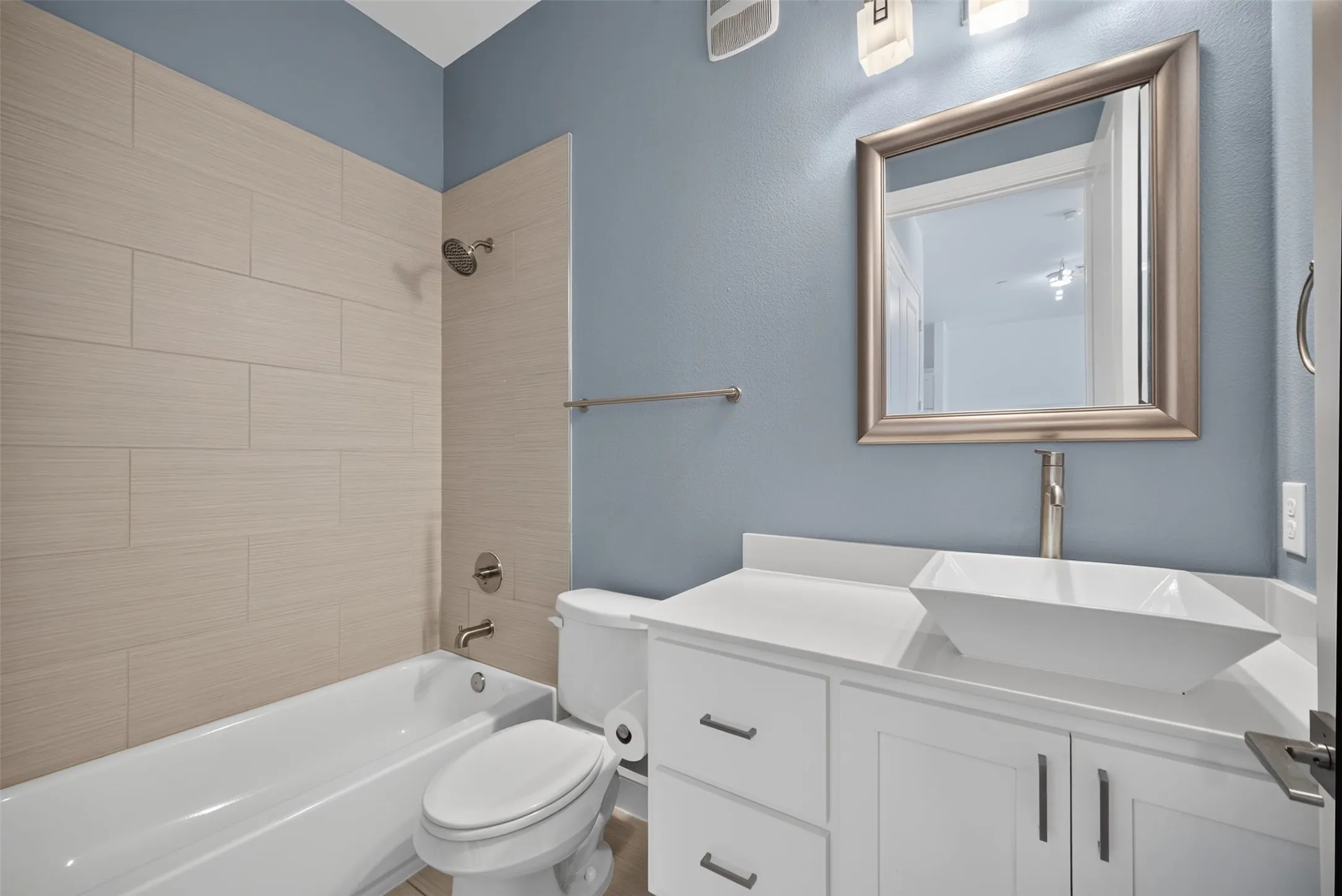 Modern bathroom featuring a freestanding vanity with a vessel sink, a brushed nickel framed mirror, white subway tile shower surround, and a tub/shower combination
