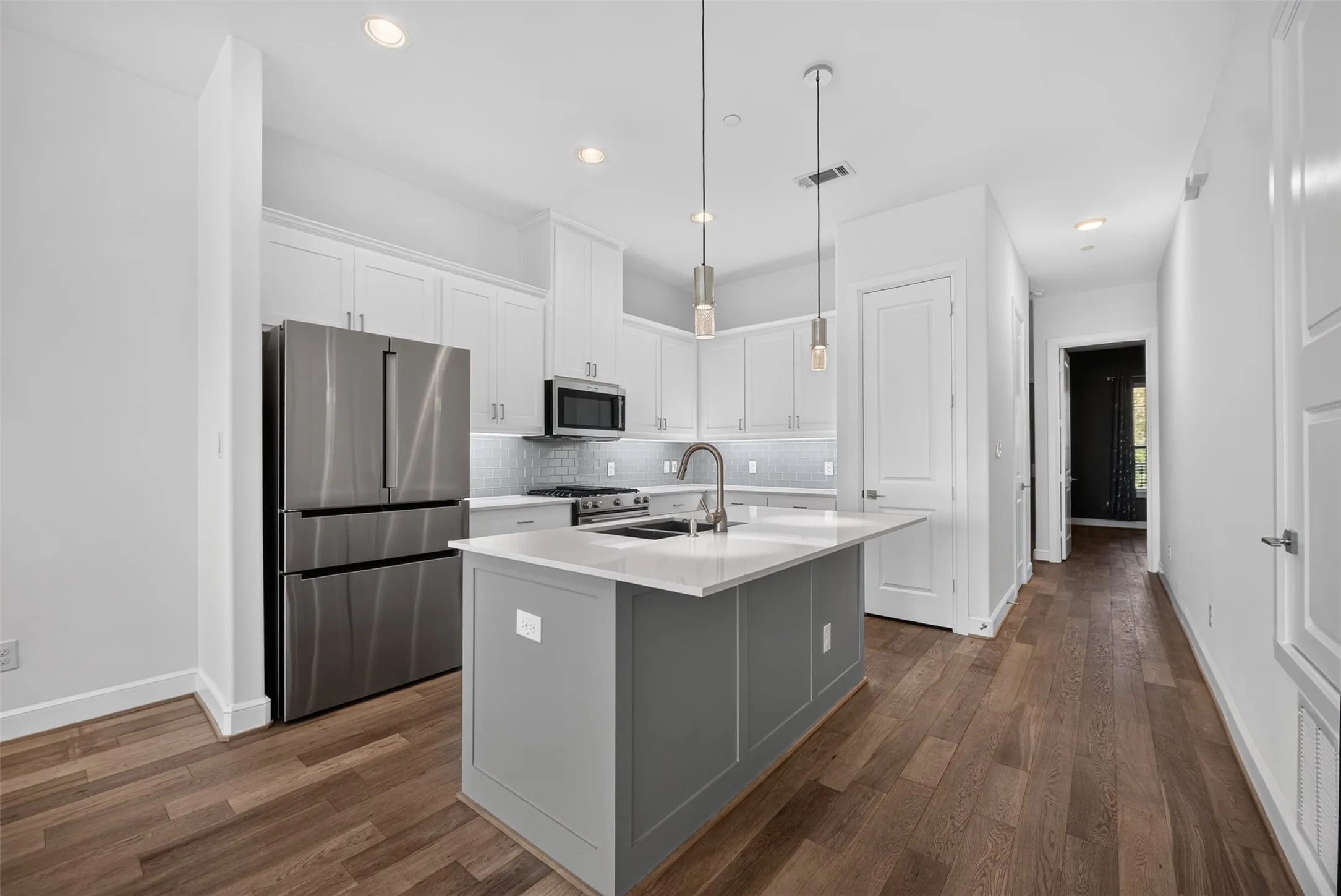Modern kitchen featuring white cabinetry, stainless steel appliances, a center island with a sink, pendant lighting, and wood-finish flooring