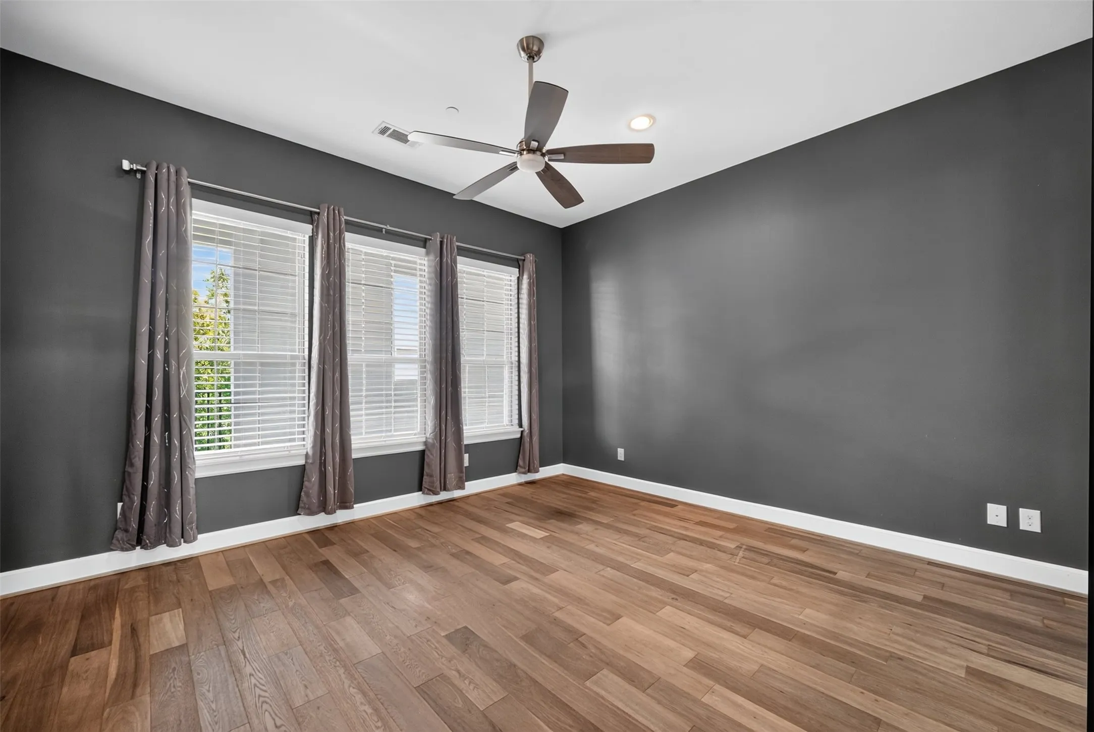 Spacious room featuring wood-finish flooring, dark-toned walls, and white trim