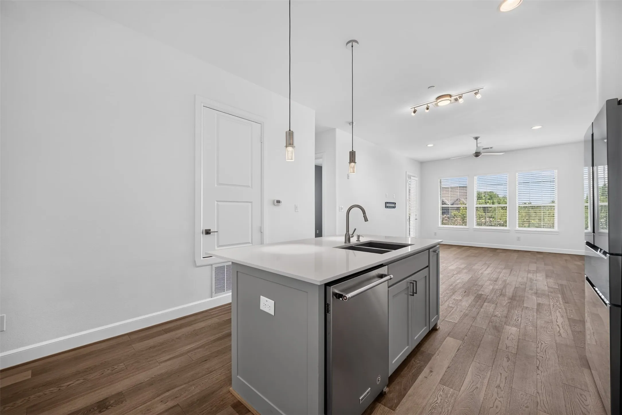 Kitchen island with light gray cabinetry, integrated stainless steel dishwasher, and a double basin sink with a high-arc faucet