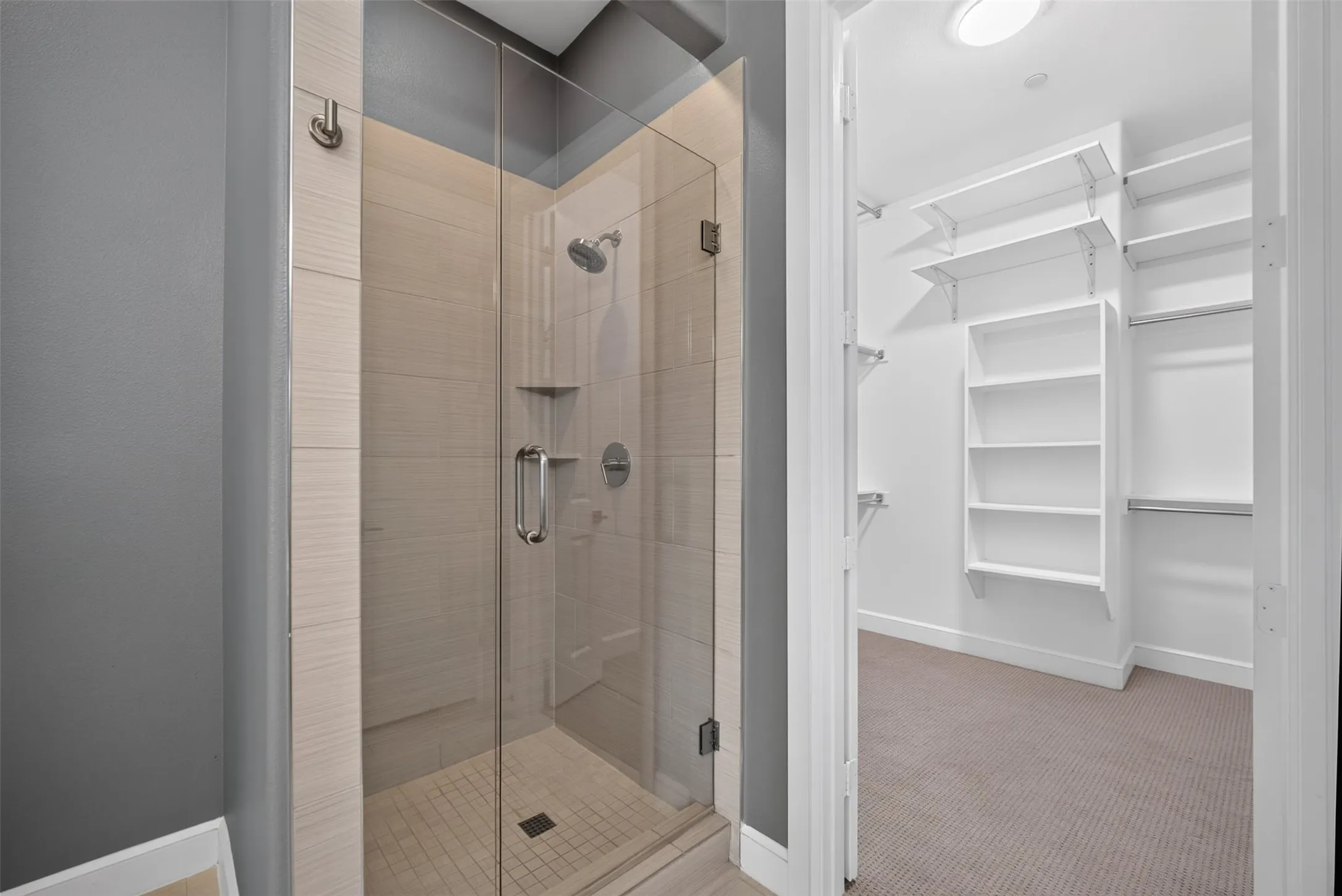 Glass-enclosed shower with tile surround and integrated shelving, featuring a chrome shower head and fixtures