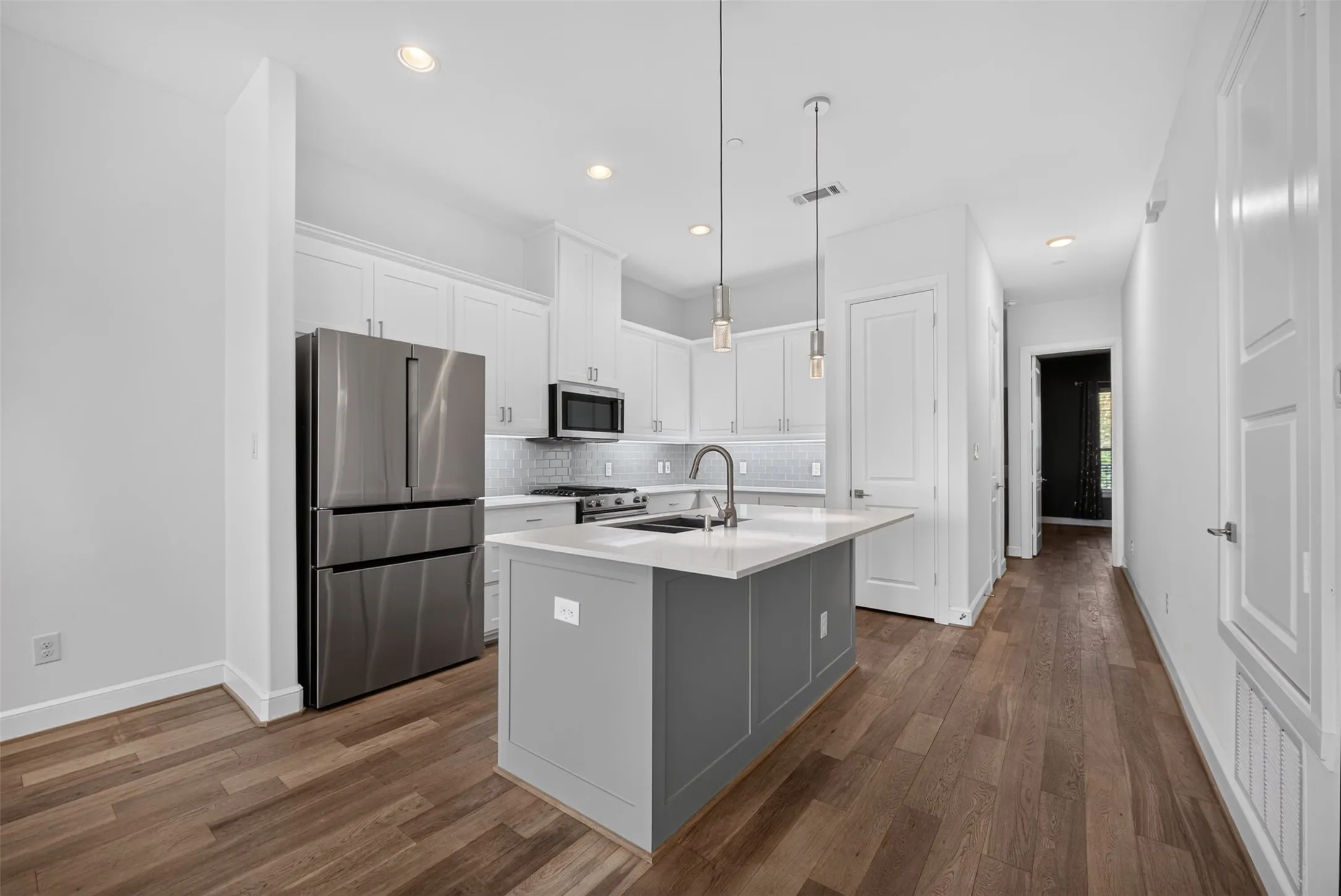 Modern kitchen featuring an island with a light-toned countertop, stainless steel appliances, white cabinetry, recessed lighting, and wood-finish flooring