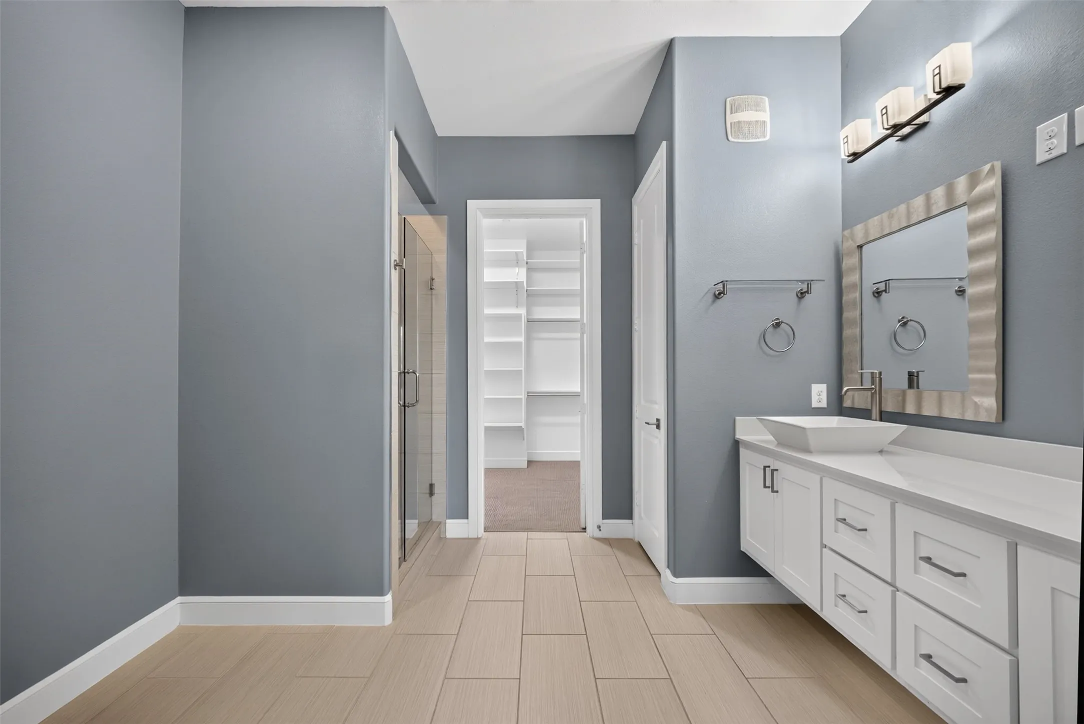 Spacious bathroom featuring light-toned tile flooring, a glass-enclosed shower, and a white floating vanity with a vessel sink