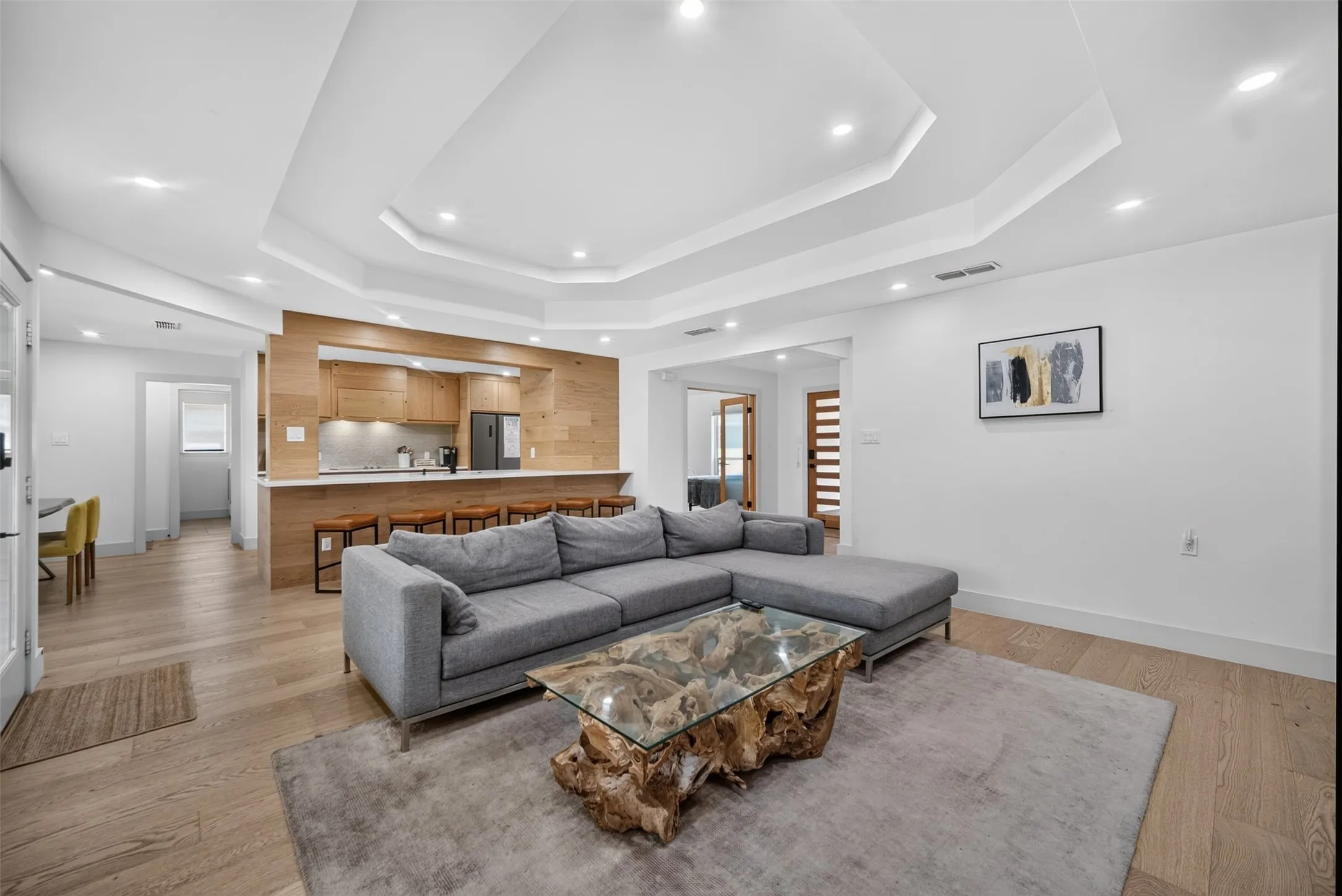 Open concept living area featuring wood-finish flooring, a tray ceiling with recessed lighting, and white baseboards
