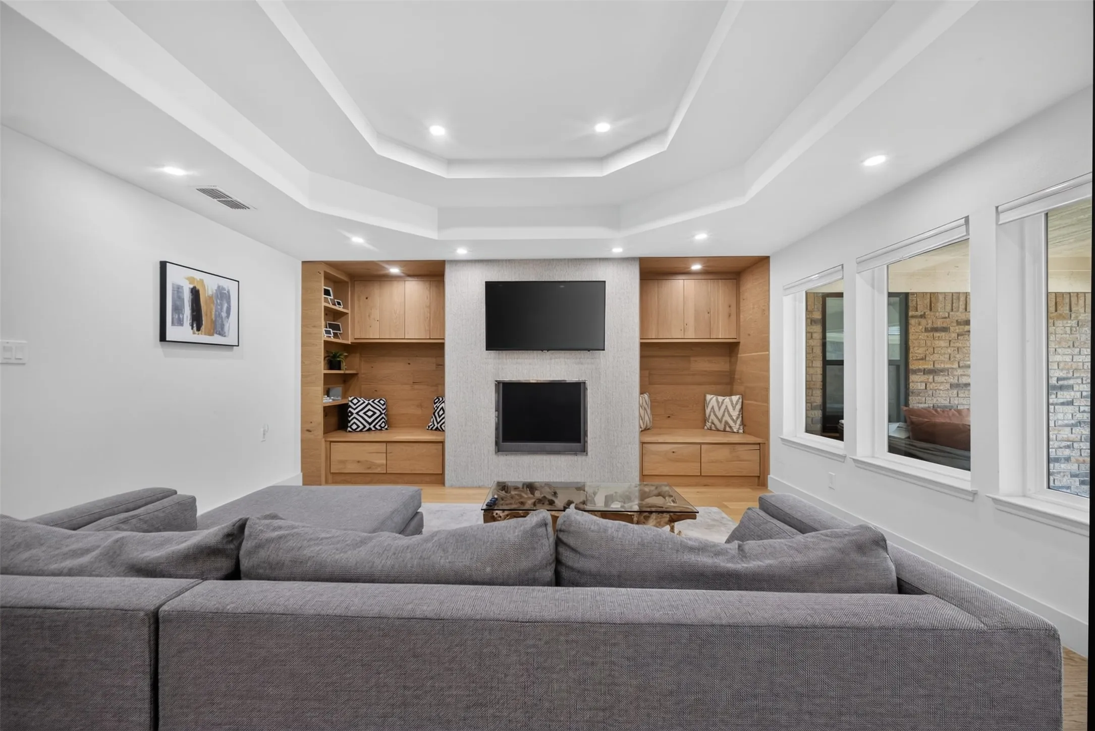 Living area featuring a tray ceiling with recessed lighting, built-in shelving, a fireplace, and multiple windows