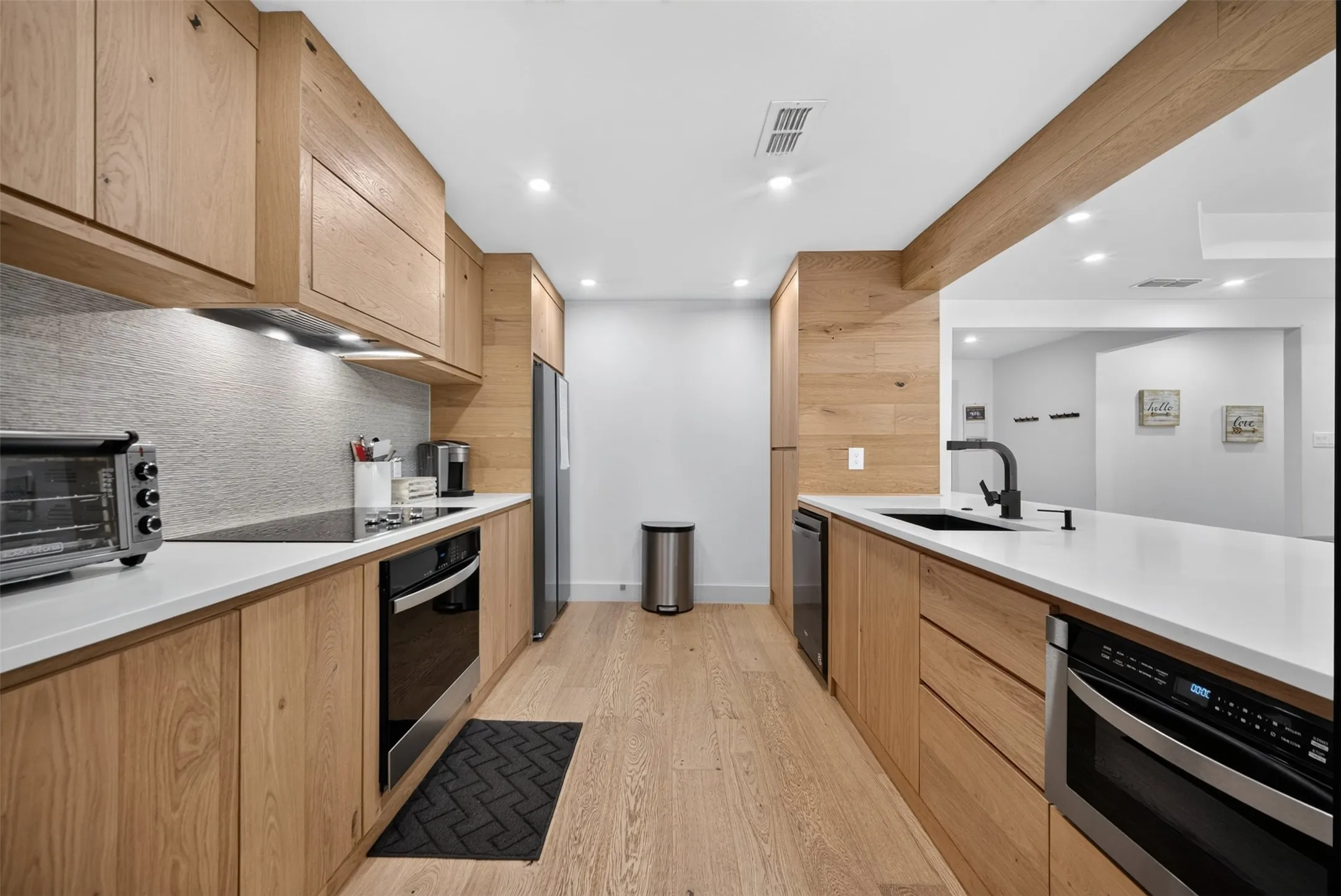 Kitchen featuring light wood-finish cabinetry, white countertops, stainless steel appliances, and wood-finish flooring