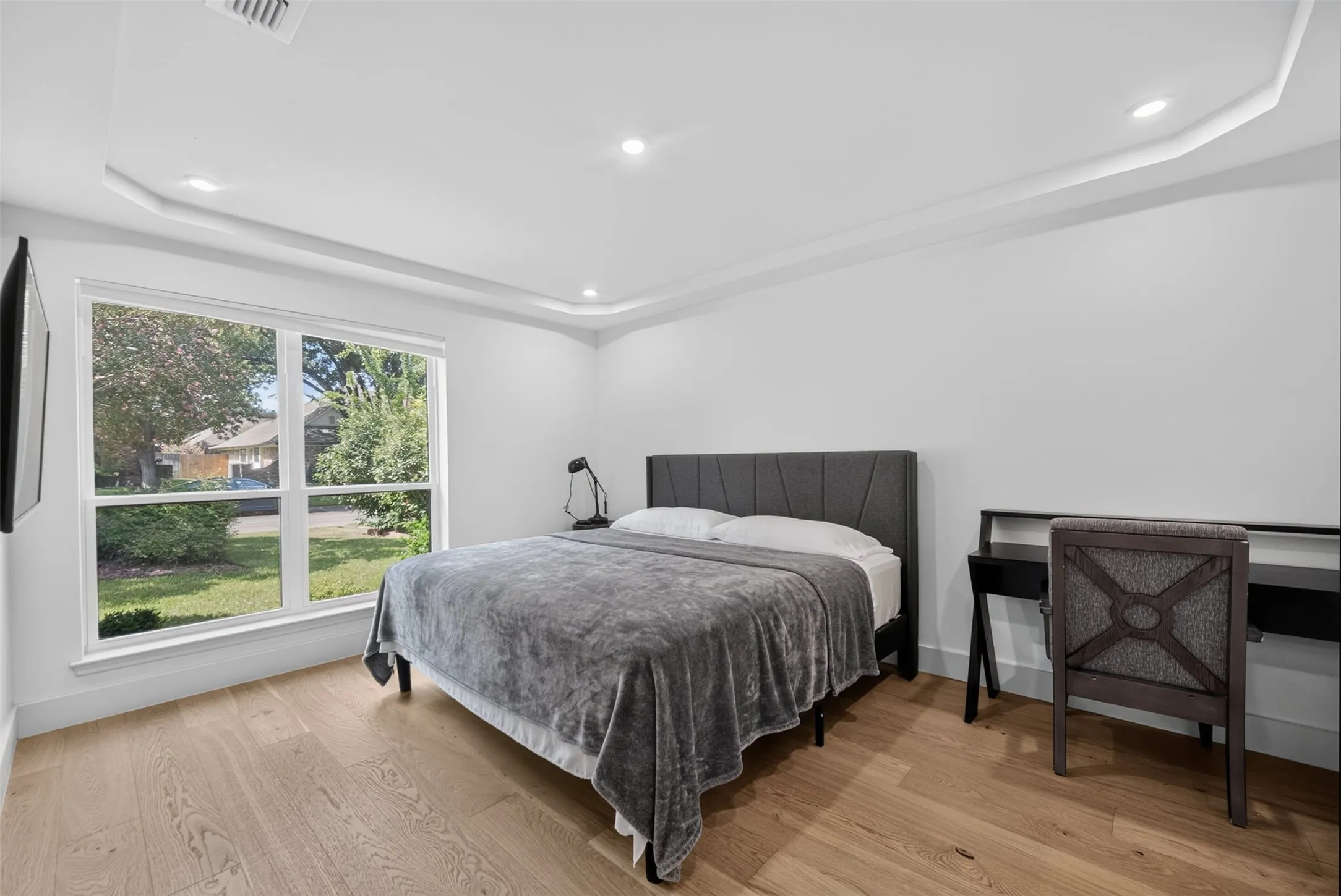 Bright room featuring a large picture window, wood-finish flooring, recessed lighting, white walls, and tray ceiling with indirect illumination