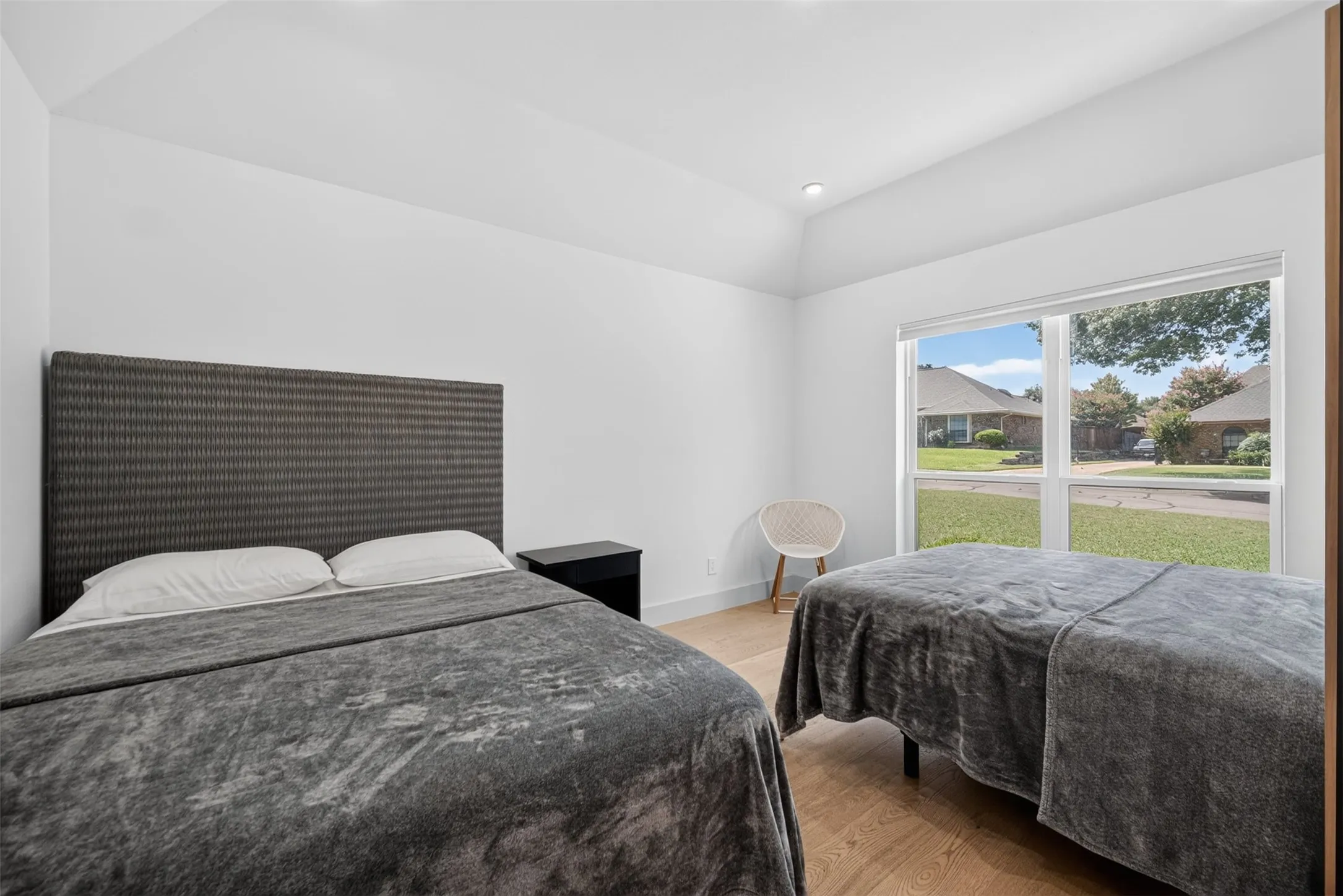 Bright room with a large window, vaulted ceiling, and light wood-finish flooring